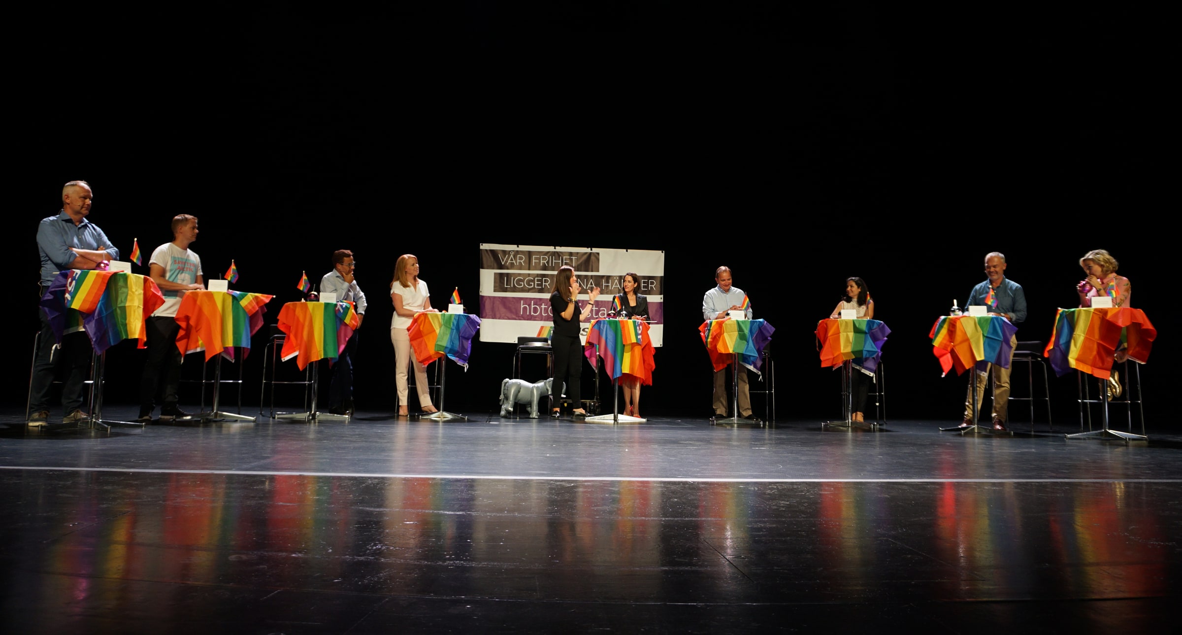Women and men stand at rainbow-covered lecterns during a Swedish party-leader debate at Stockholm Pride.
