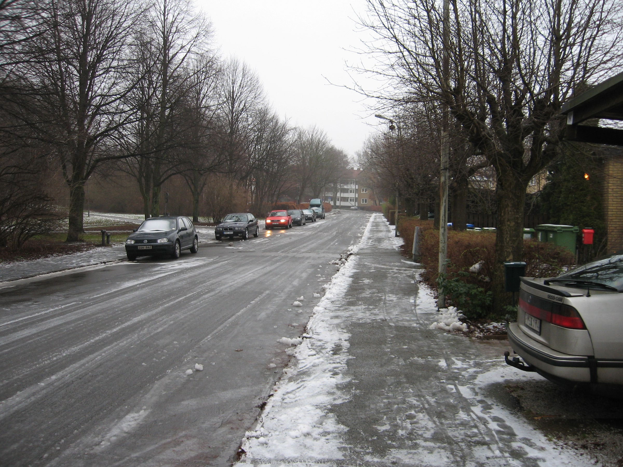 Cars travel along a road with slush beside the pavement in Lund, Sweden.