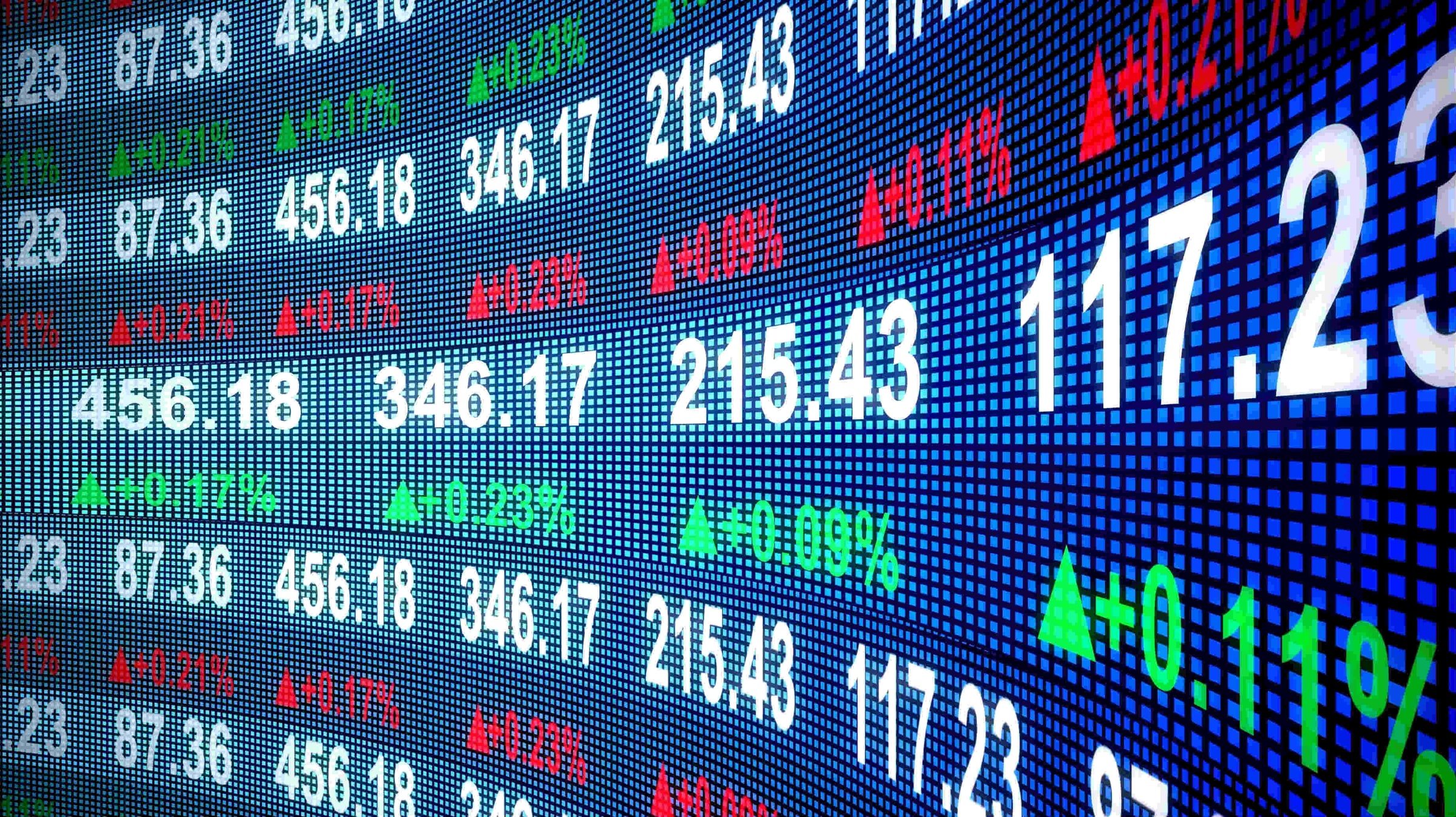 An electronic market board displays changing share prices and percentage movements.