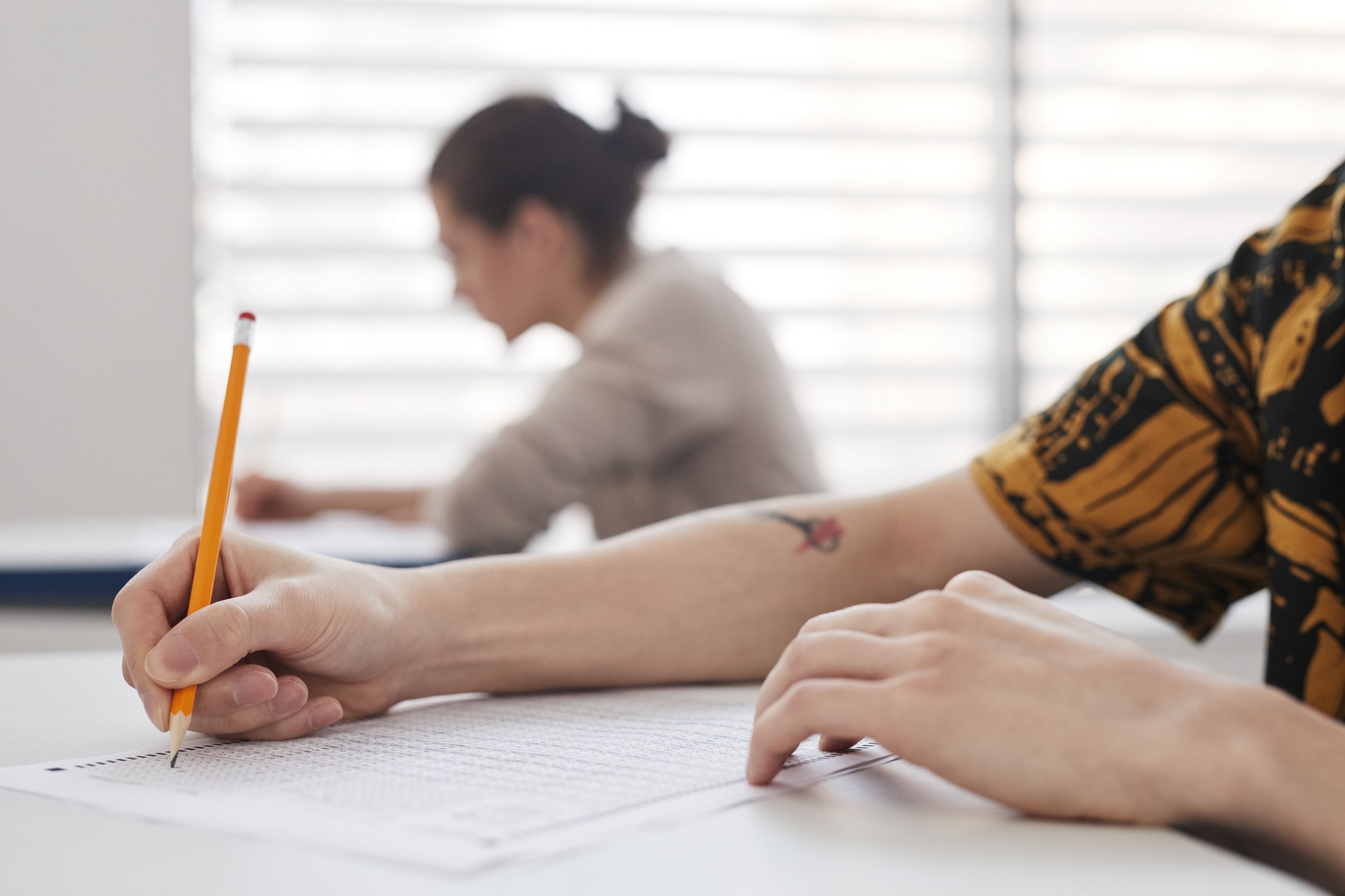 A person writes on an exam sheet with a pencil at a desk.