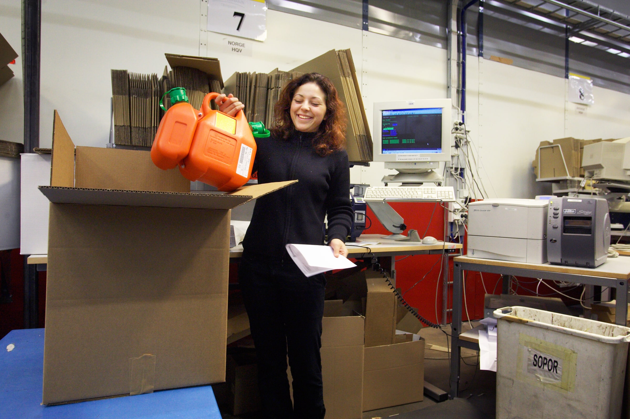 A warehouse worker in Sweden packs two orange containers into an open cardboard box.
