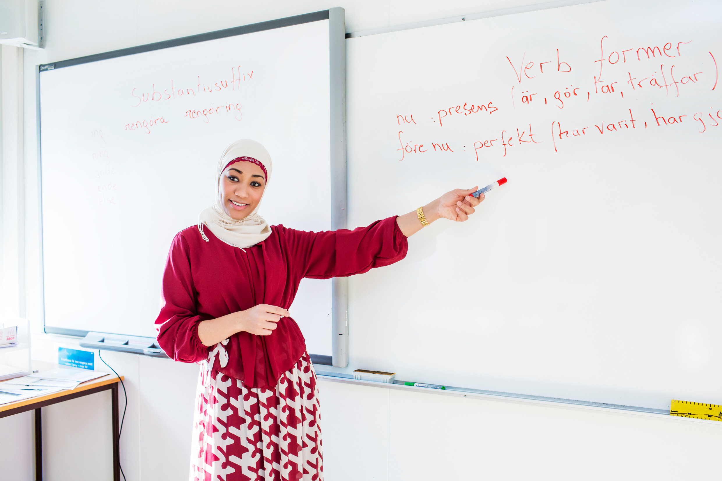 A woman points to Swedish grammar on a classroom whiteboard.