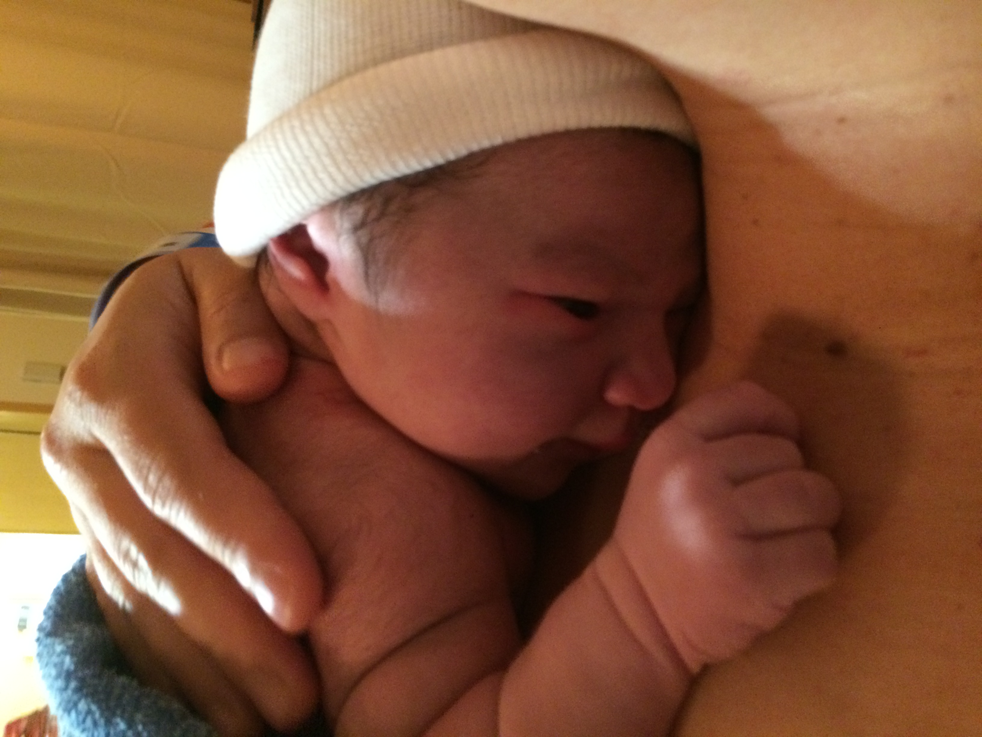 A newborn baby held skin to skin on a parent's chest with the baby's face visible