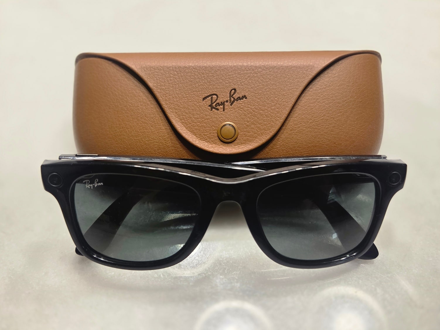 Black Ray-Ban Meta smart glasses sit in front of their brown charging case.