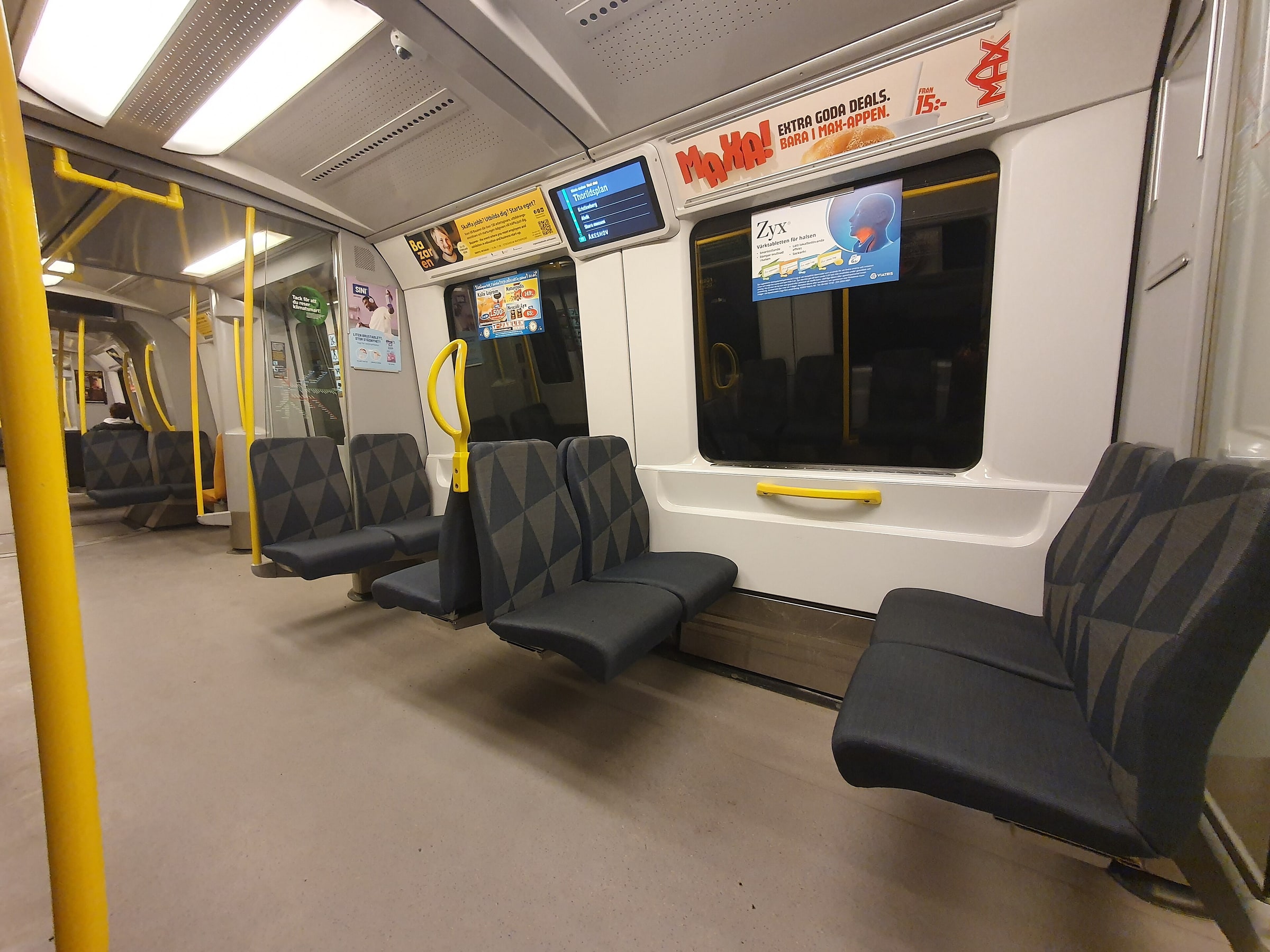 Inside a Stockholm metro carriage with grey seats, yellow handrails and a display showing Thorildsplan.