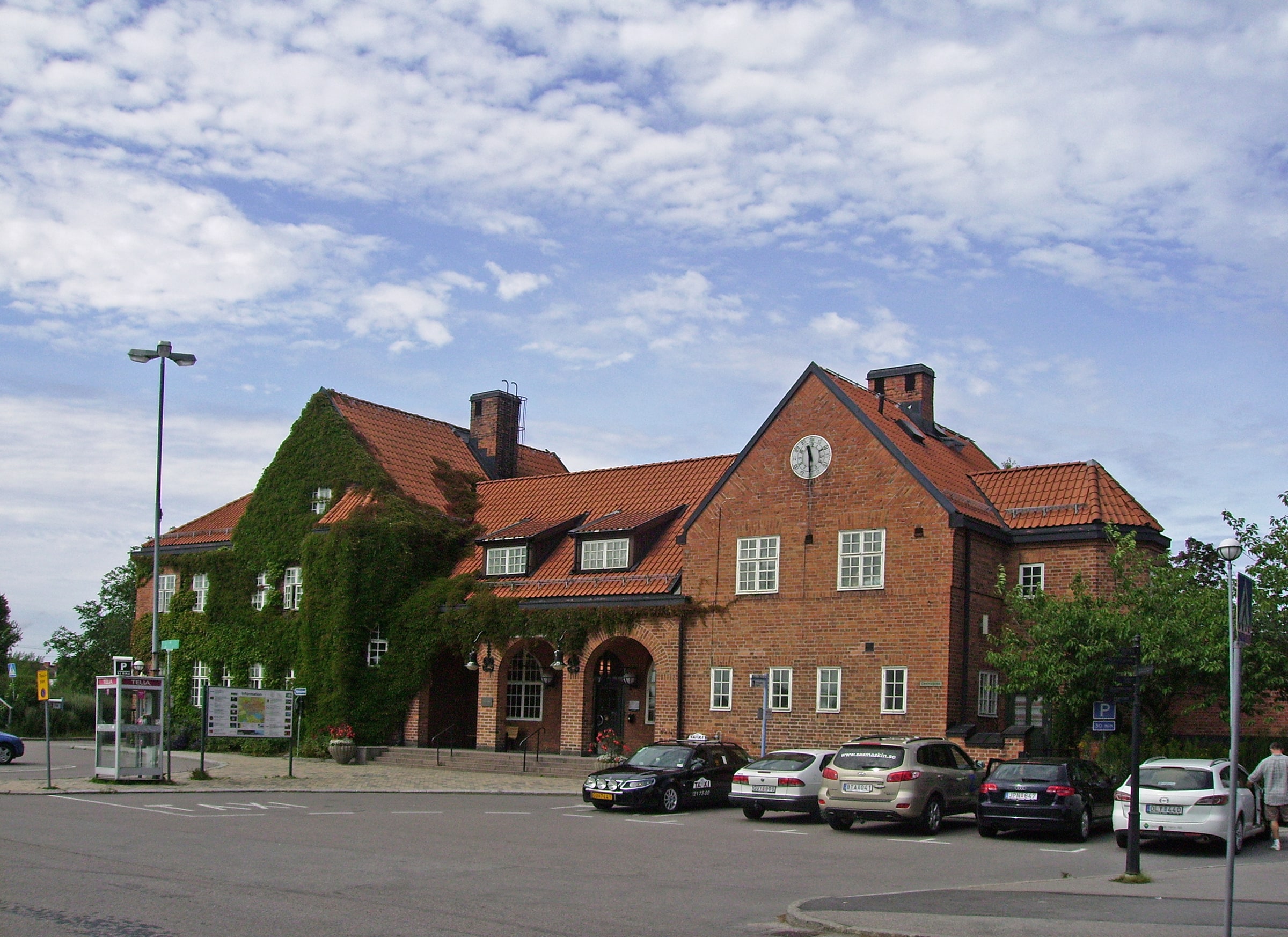 The brick Nyköping railway station building beside its forecourt under a partly cloudy sky.