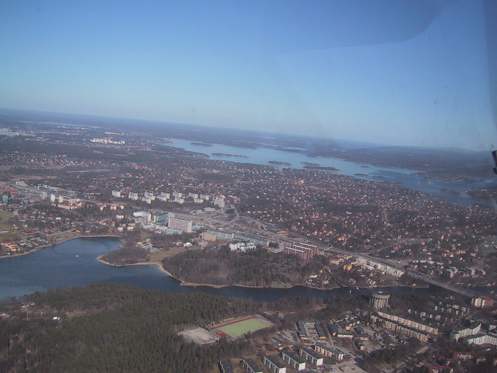 An aerial view across apartment blocks, houses, roads, woodland and water north of central Stockholm.
