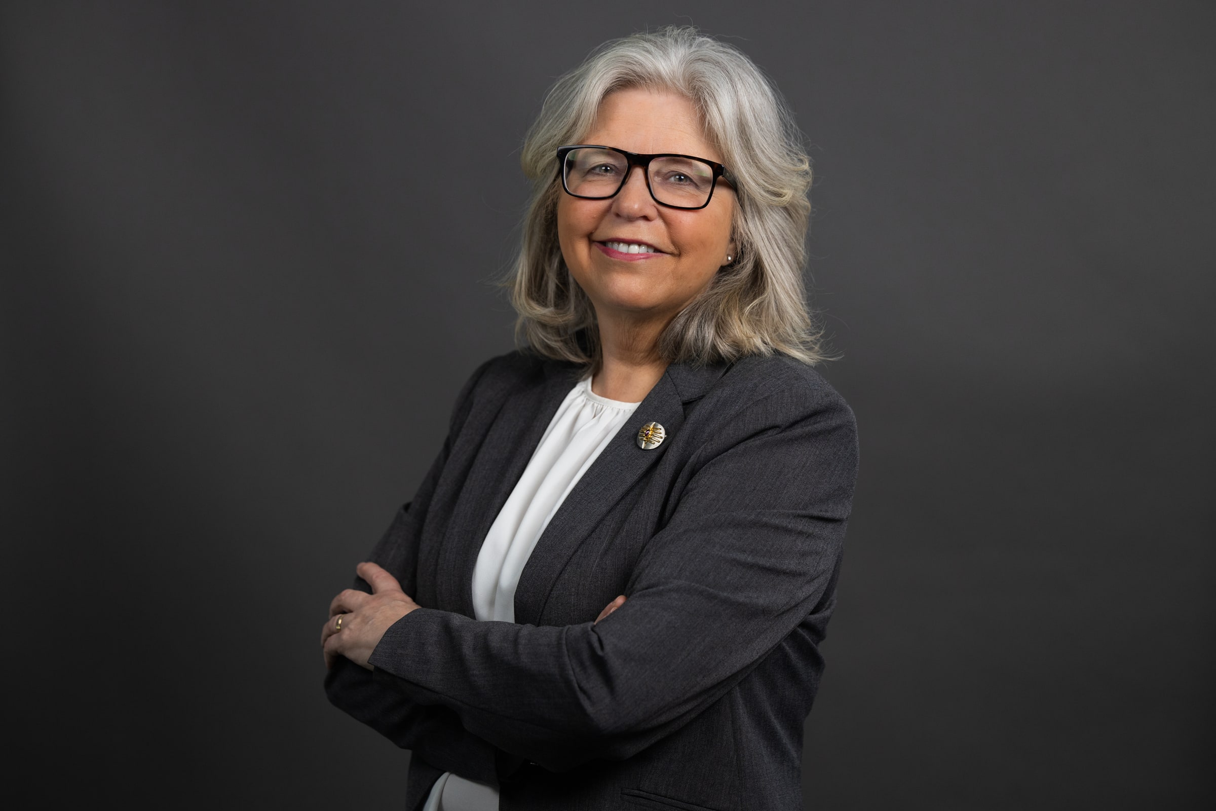Maria Mindhammar wearing glasses and a dark jacket against a grey background