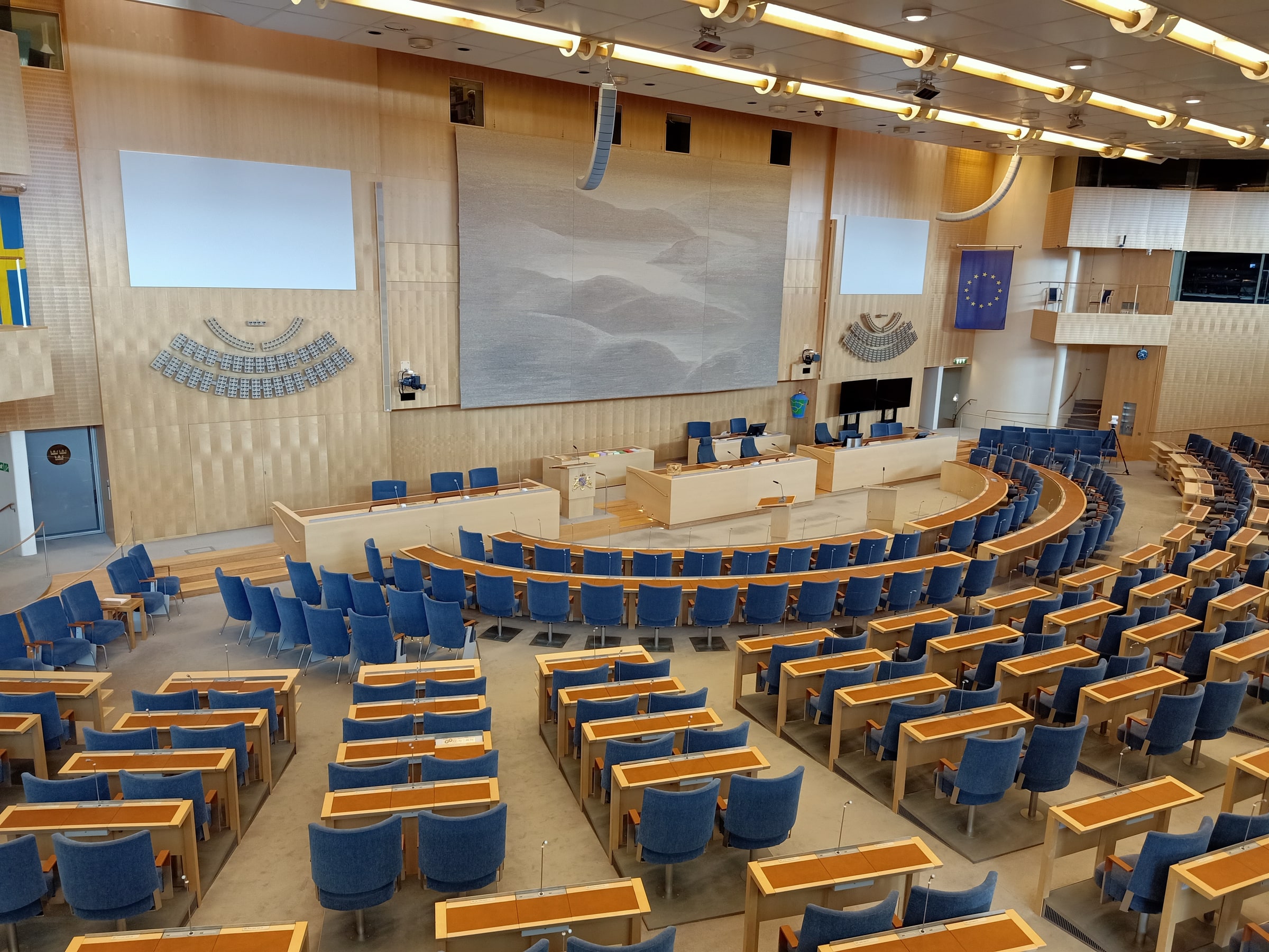 The Swedish Parliament chamber with curved blue seating and lecterns, photographed on 14 August 2019.