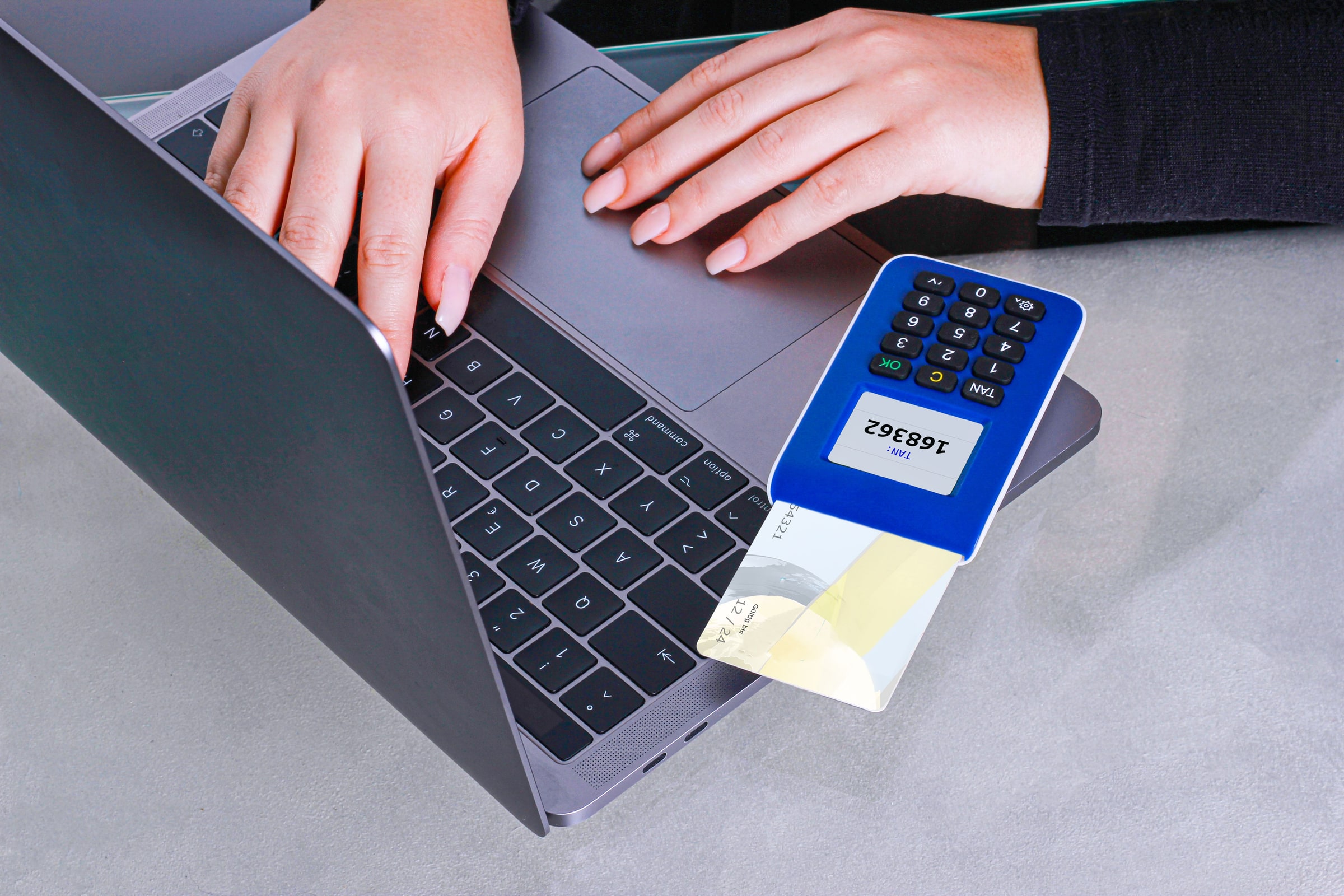 A person uses a card reader beside a laptop for an online financial transaction.