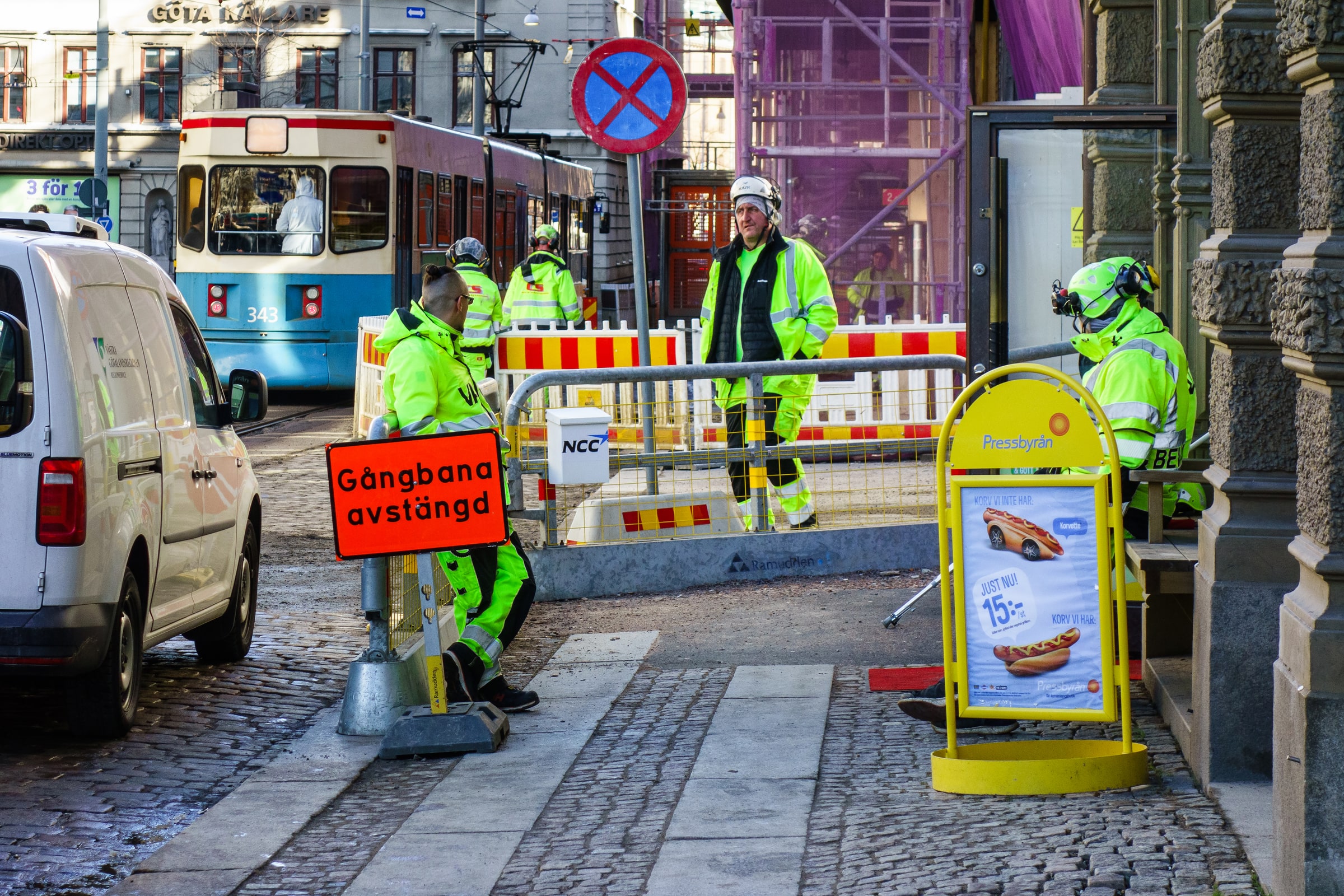 Construction workers in high-visibility clothing move a safety barrier beside a Gothenburg pavement.