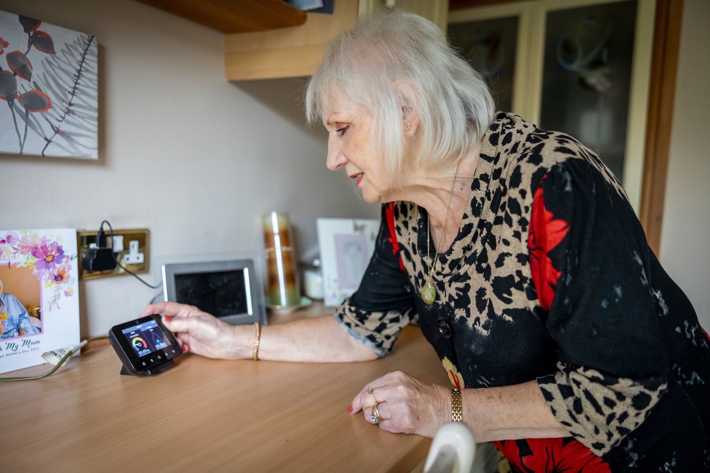 A woman leans over a desk to check a home energy monitor.