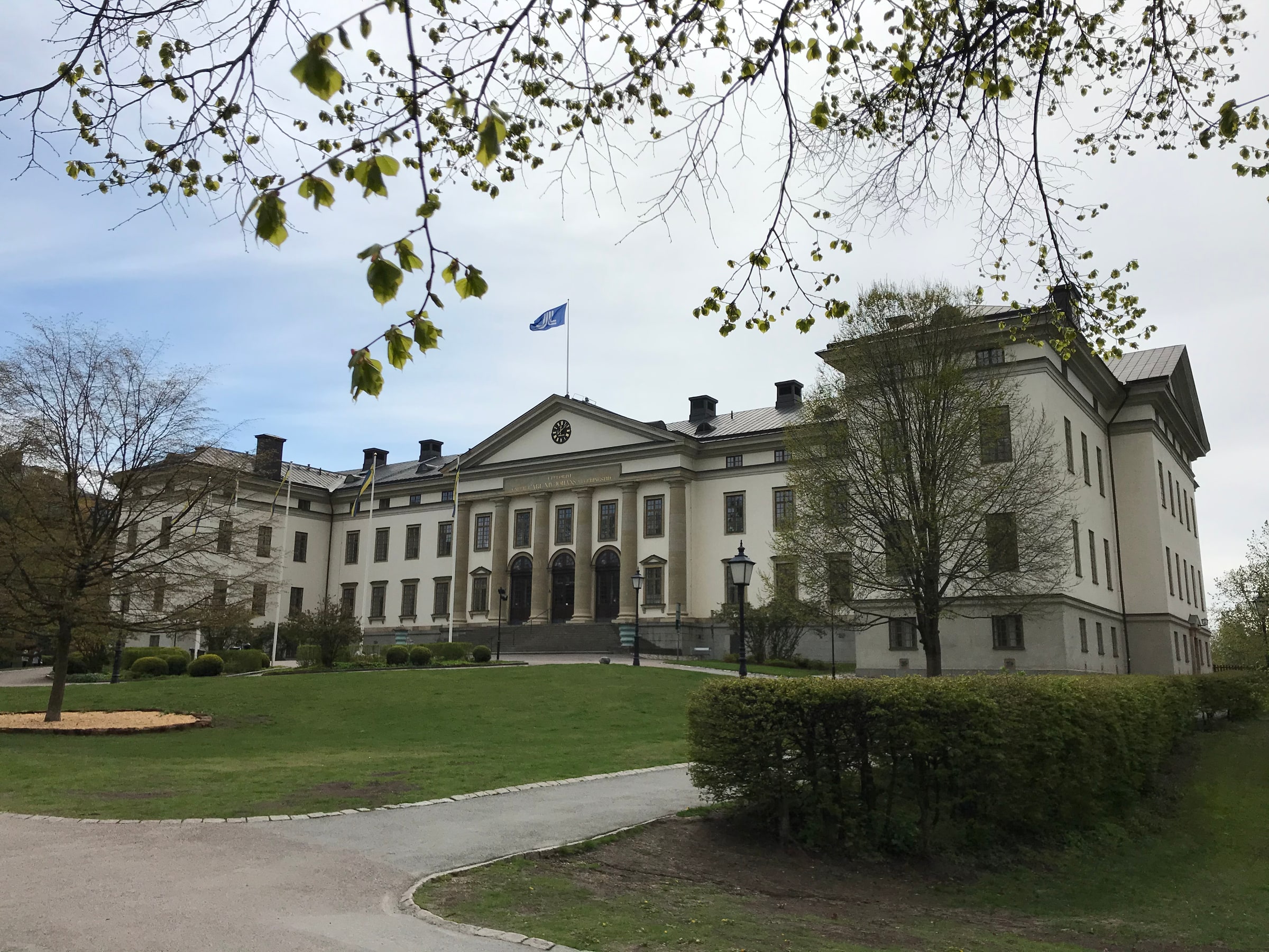 Landstingshuset’s pale facade, central entrance and pediment, with a lawn and trees. No people or meeting are visible.