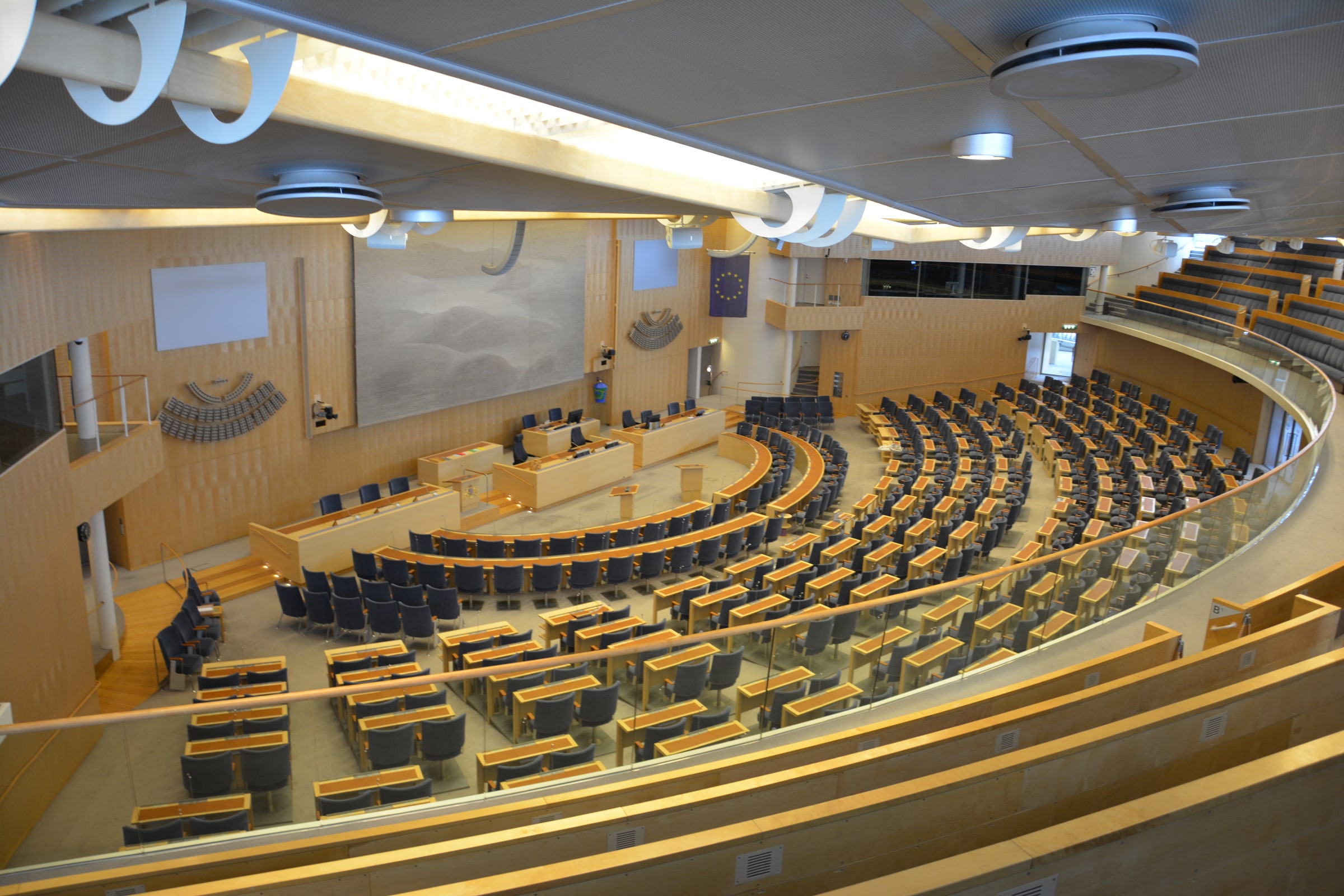 Blue seats and curved desks face the presiding table in Sweden’s Parliament chamber.