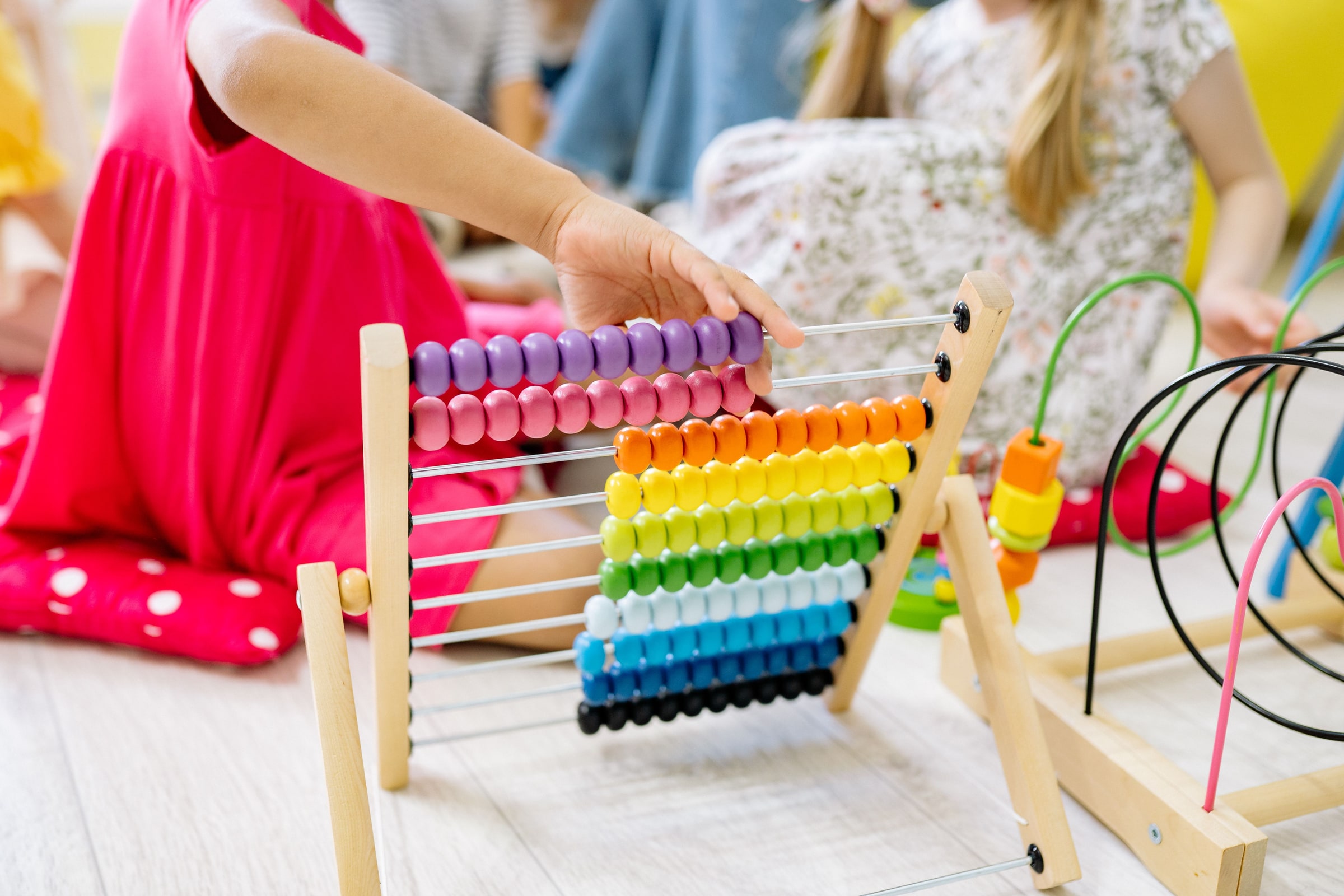 Child's hand manipulating a wooden abacus; other children's torsos and an educational bead toy.