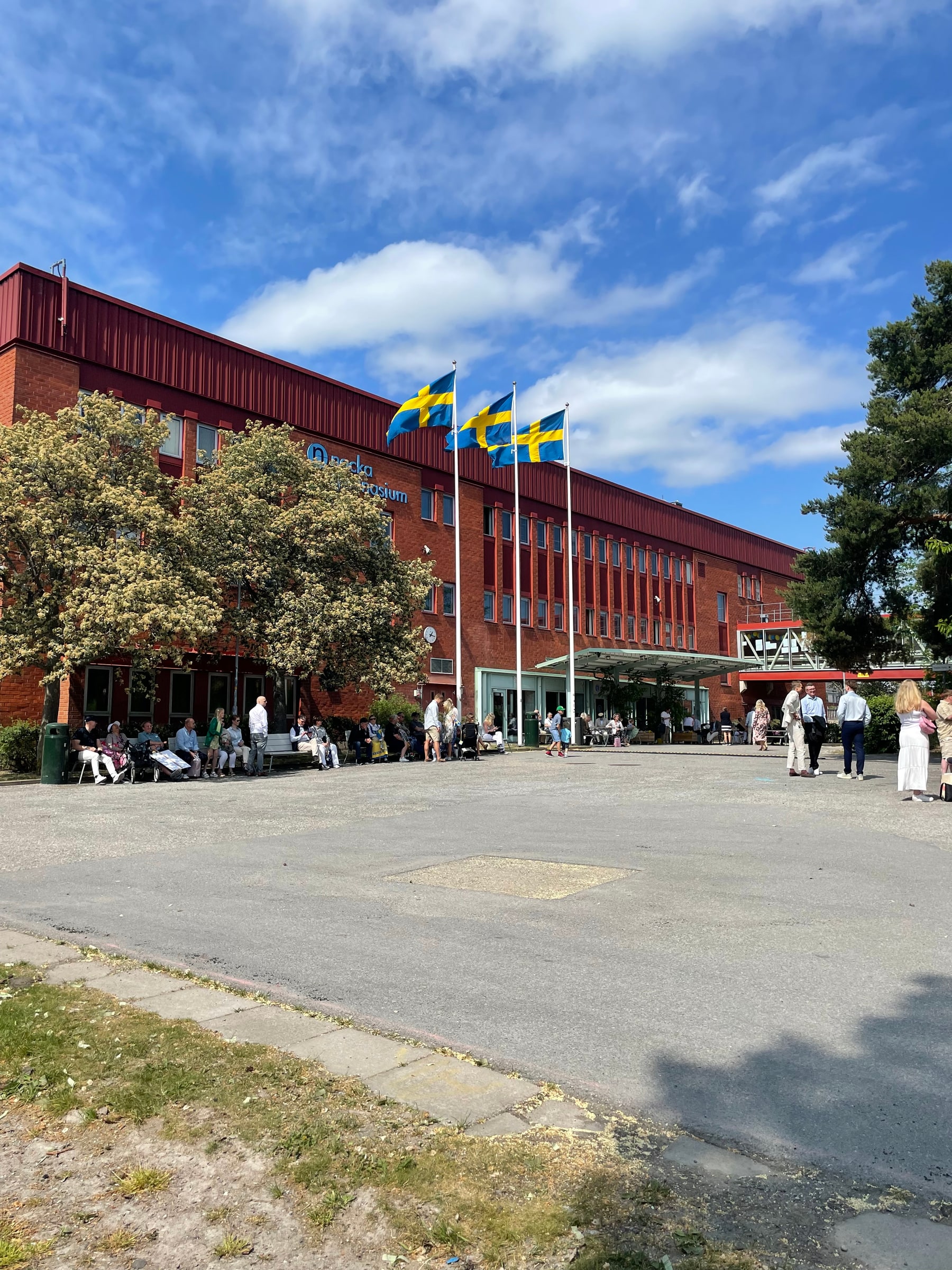 People gathered outside Nacka gymnasium beneath Swedish flags