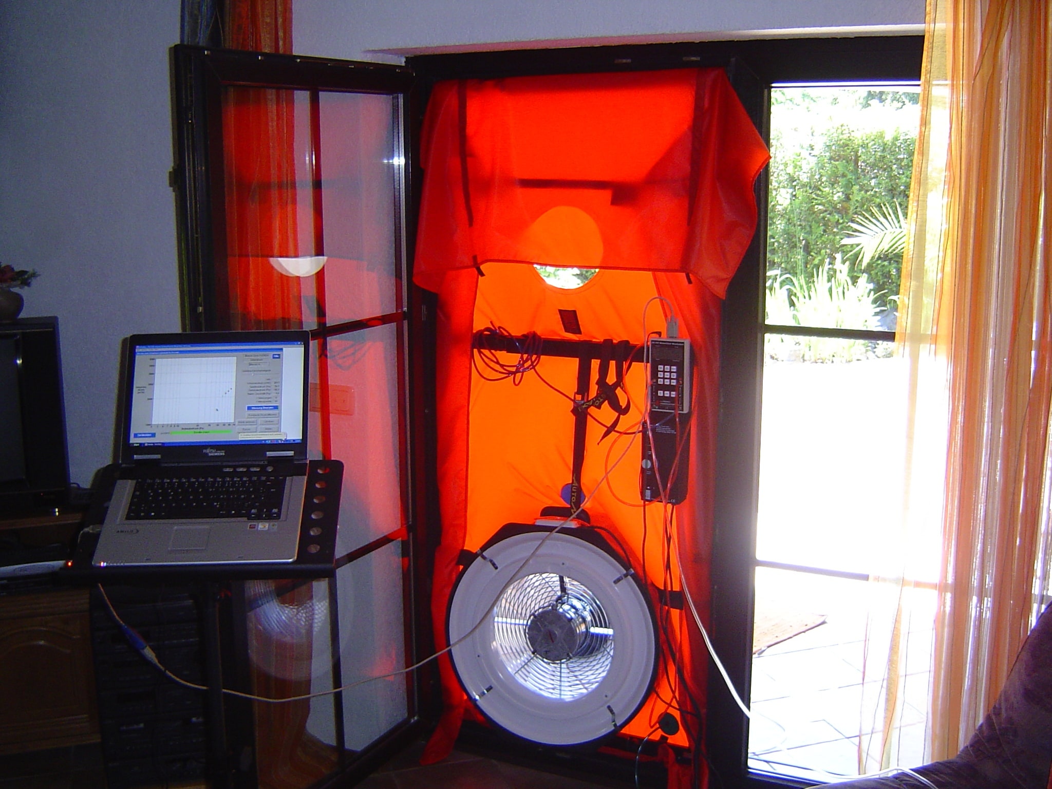 A blower-door test fan and measuring instruments installed in a building doorway.
