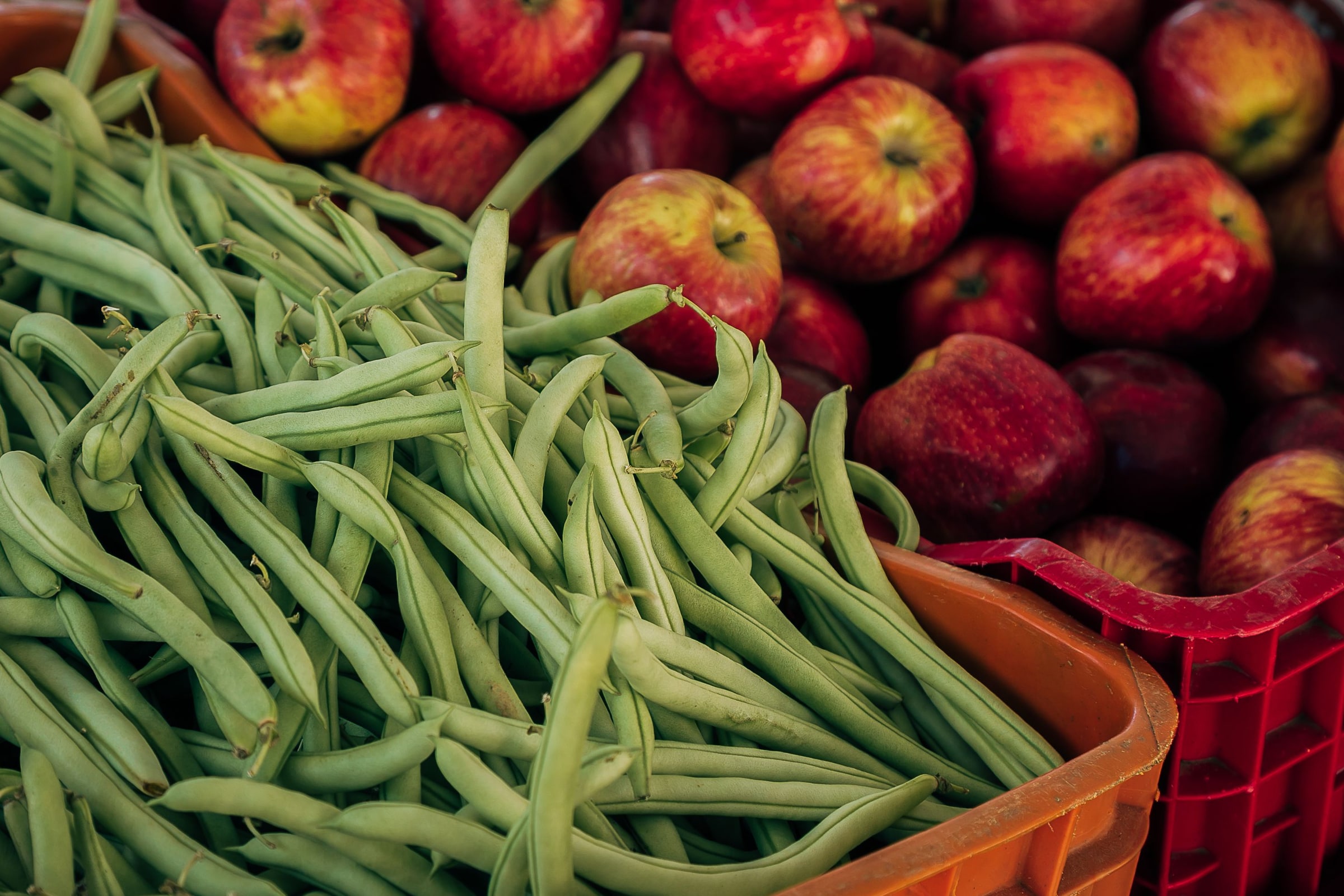 Green beans and red apples displayed in crates at a produce market.