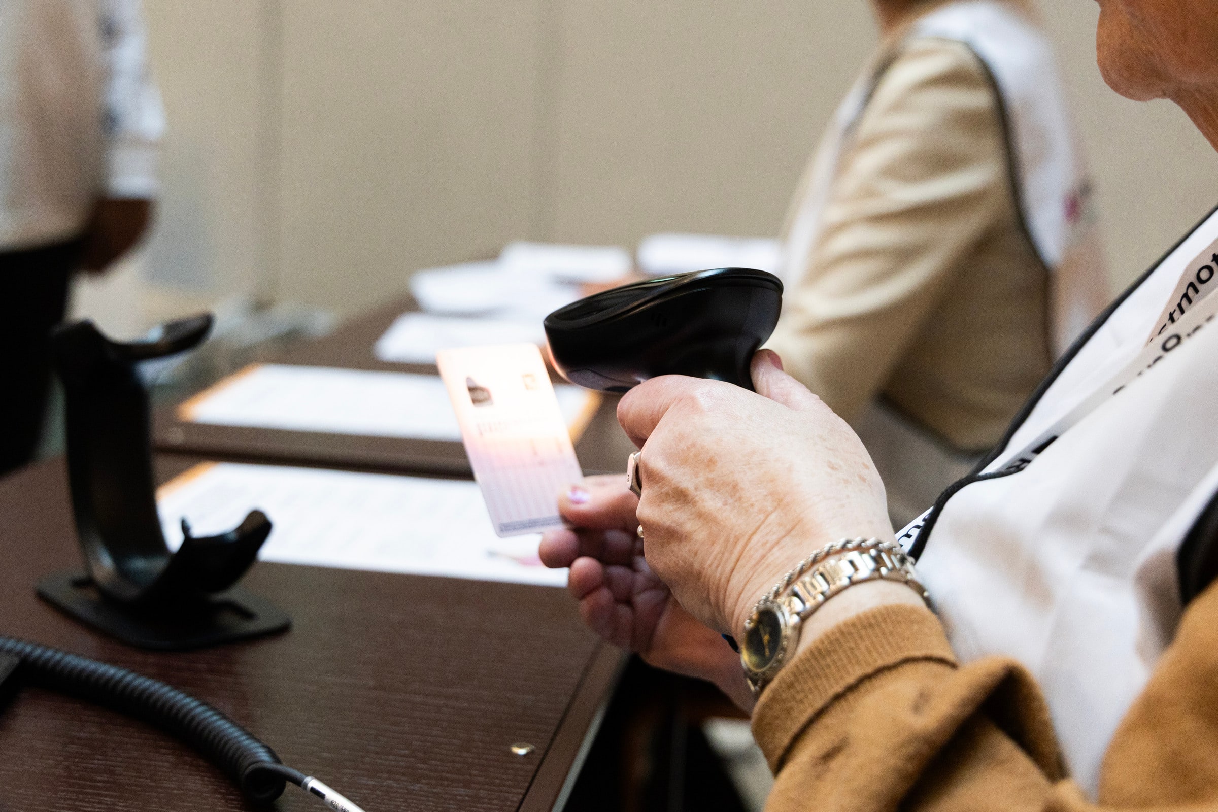 An election worker scans an identity card with a handheld scanner at an early-voting desk.