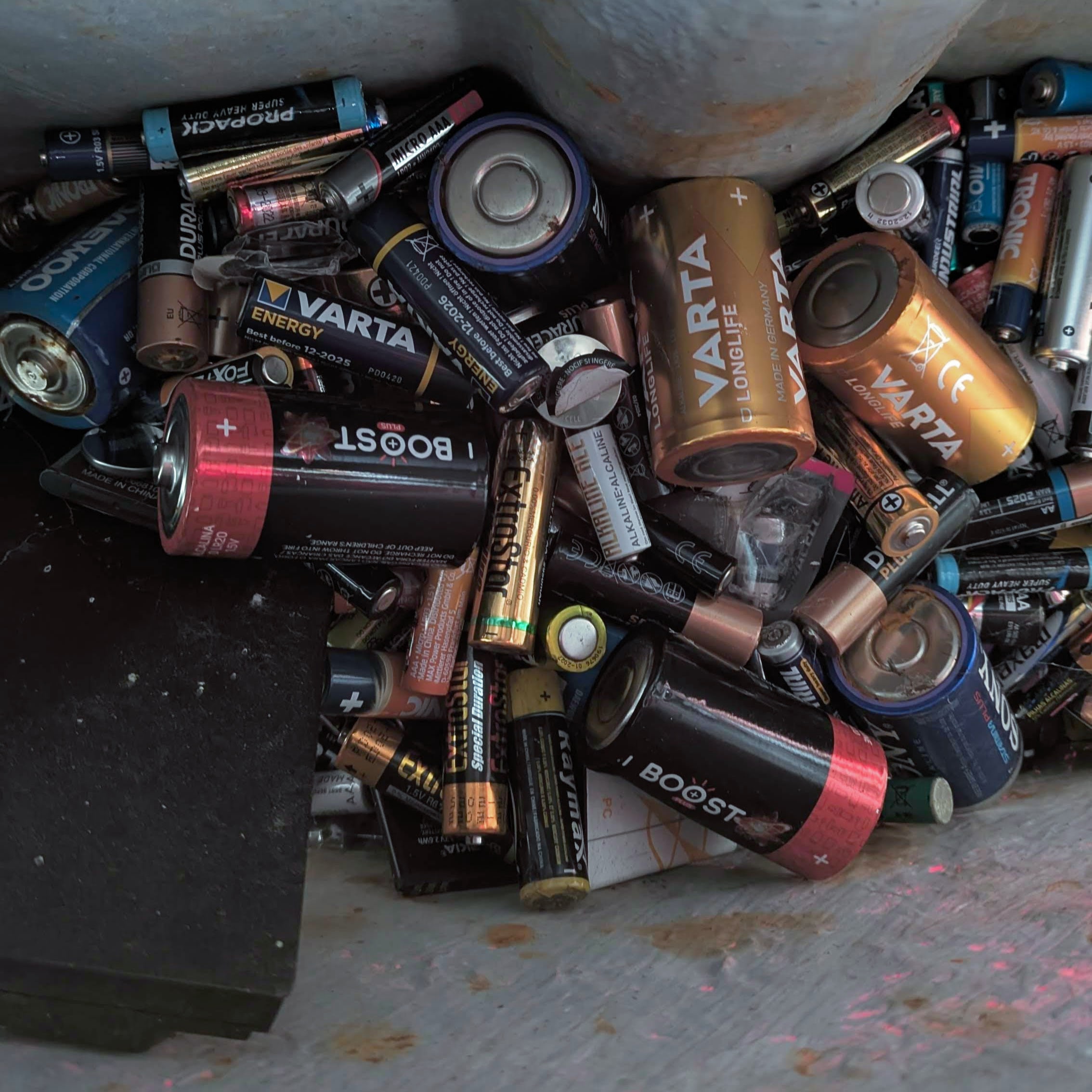 Used household batteries piled inside a dedicated battery collection container.