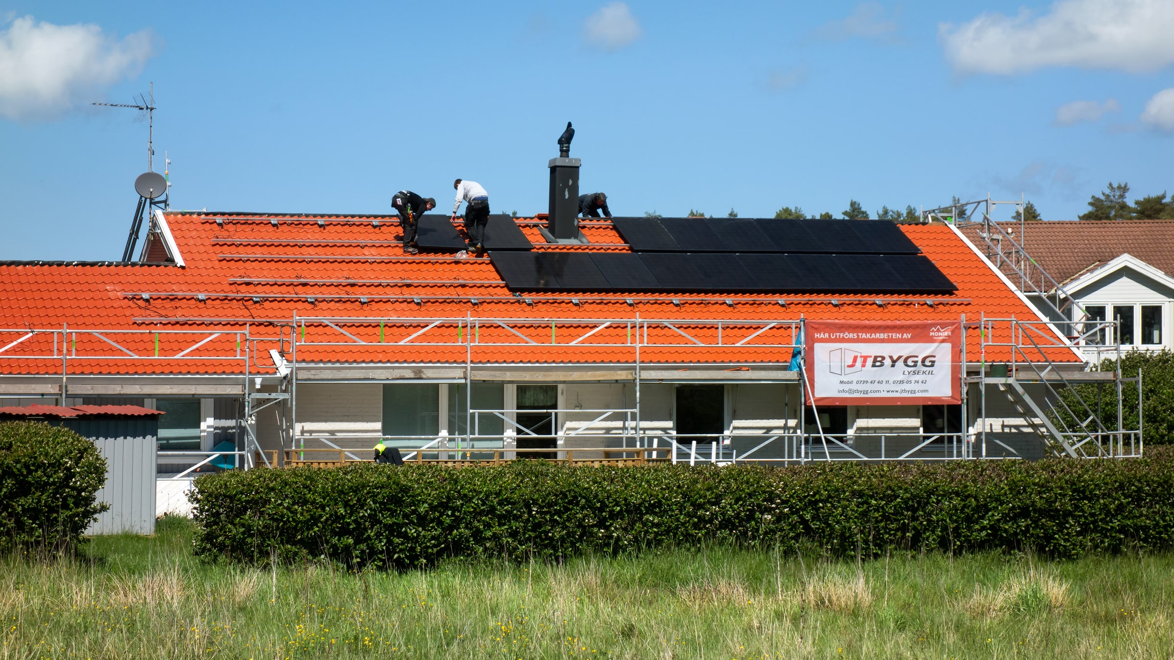 Three workers install solar panels on a red-tiled house in Brastad, Sweden.