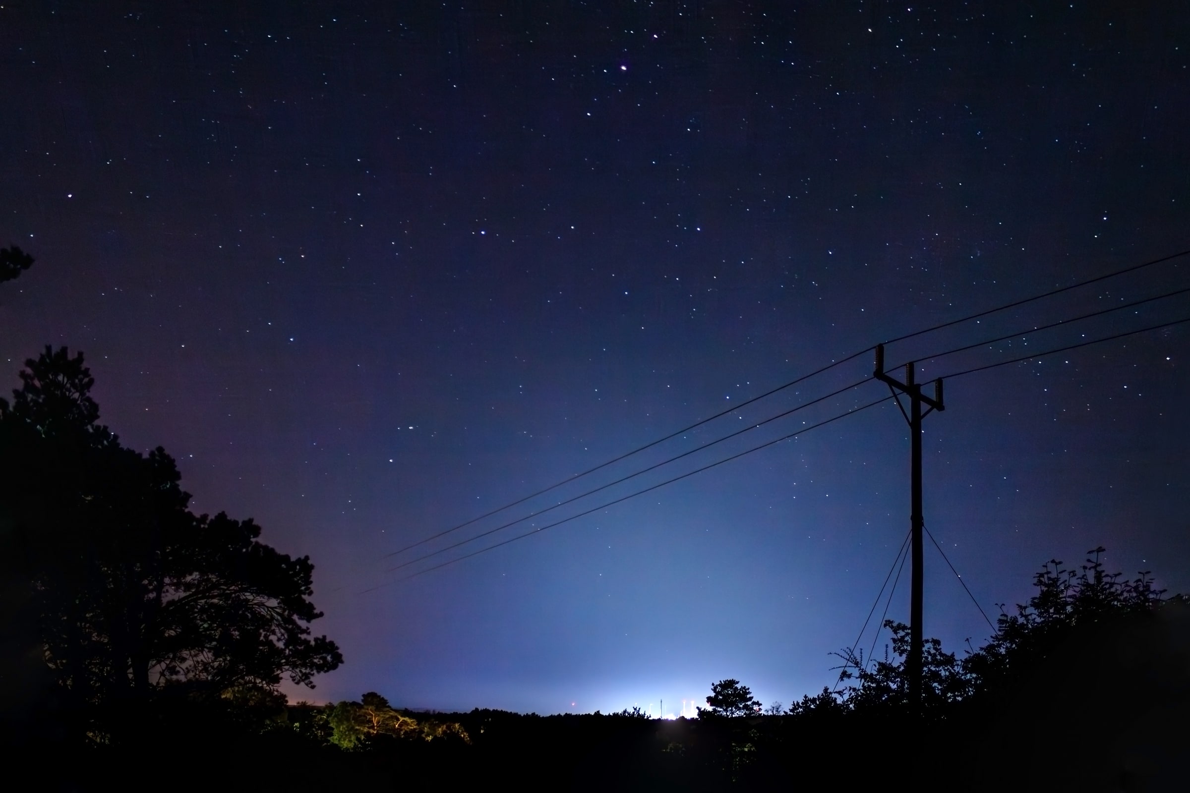 Light from the Preemraff refinery glows behind trees in Lysekil Municipality at night.