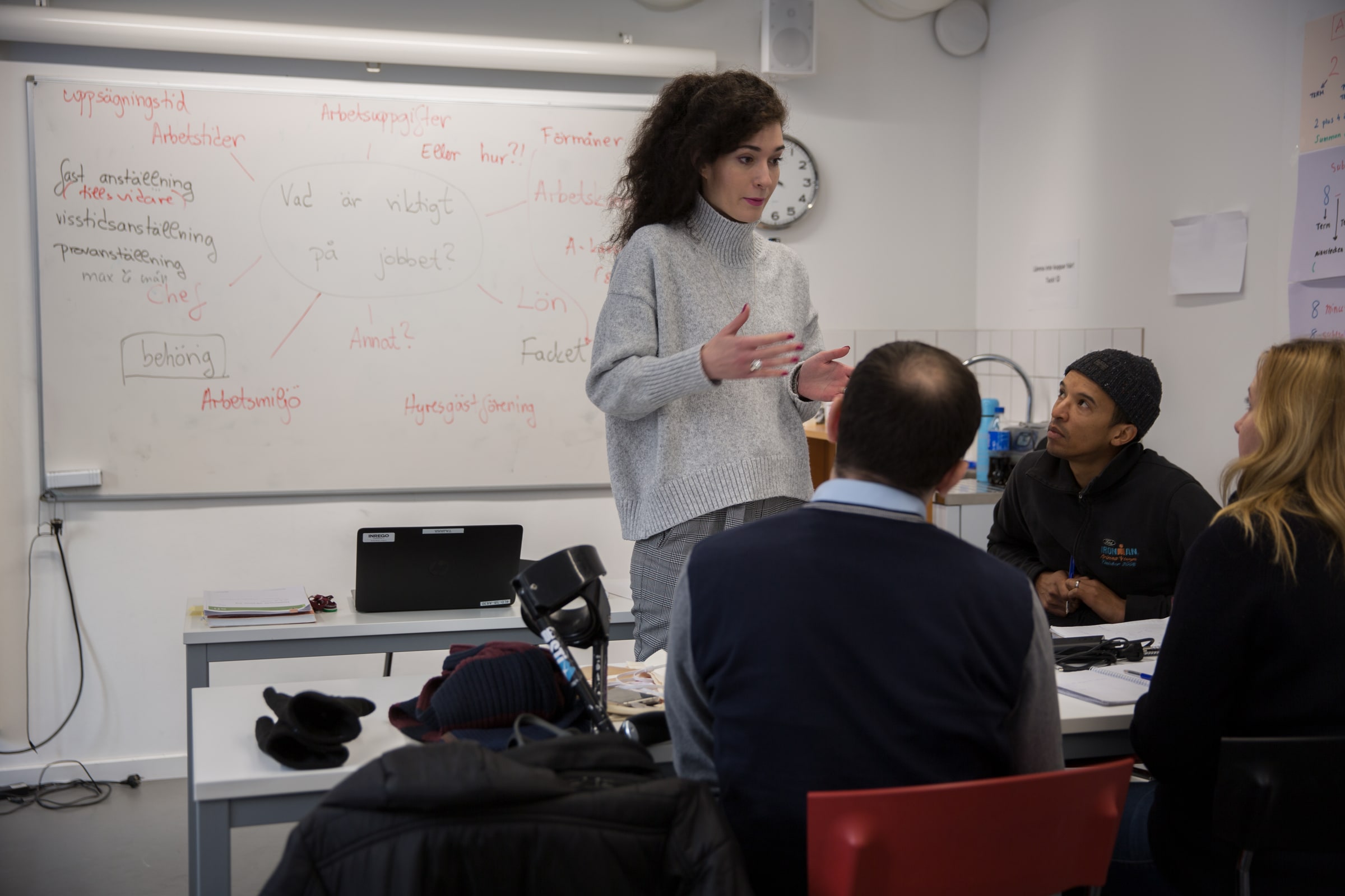 A teacher stands beside a whiteboard while adult learners sit around classroom tables in Lund.