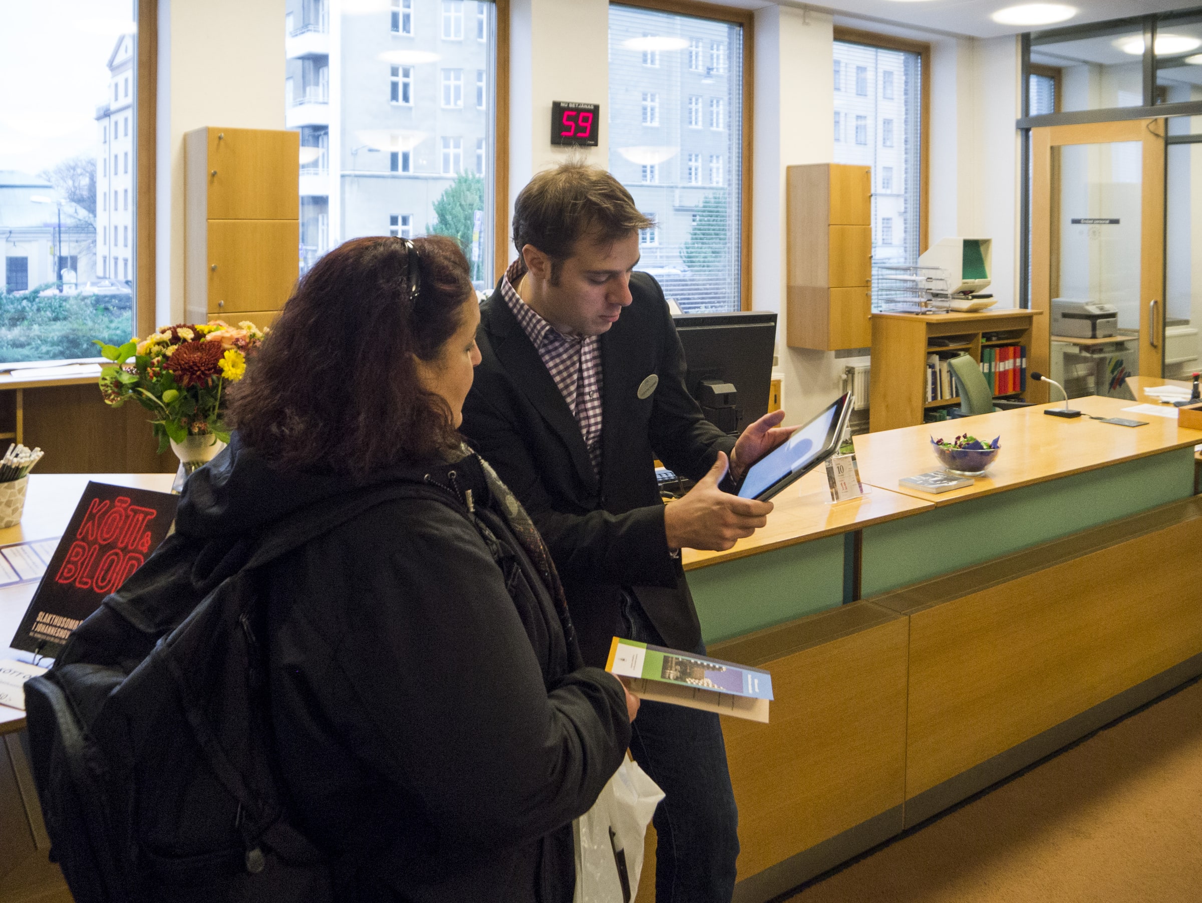 Two people look at a tablet beside Stockholm City Archives’ service counter.
