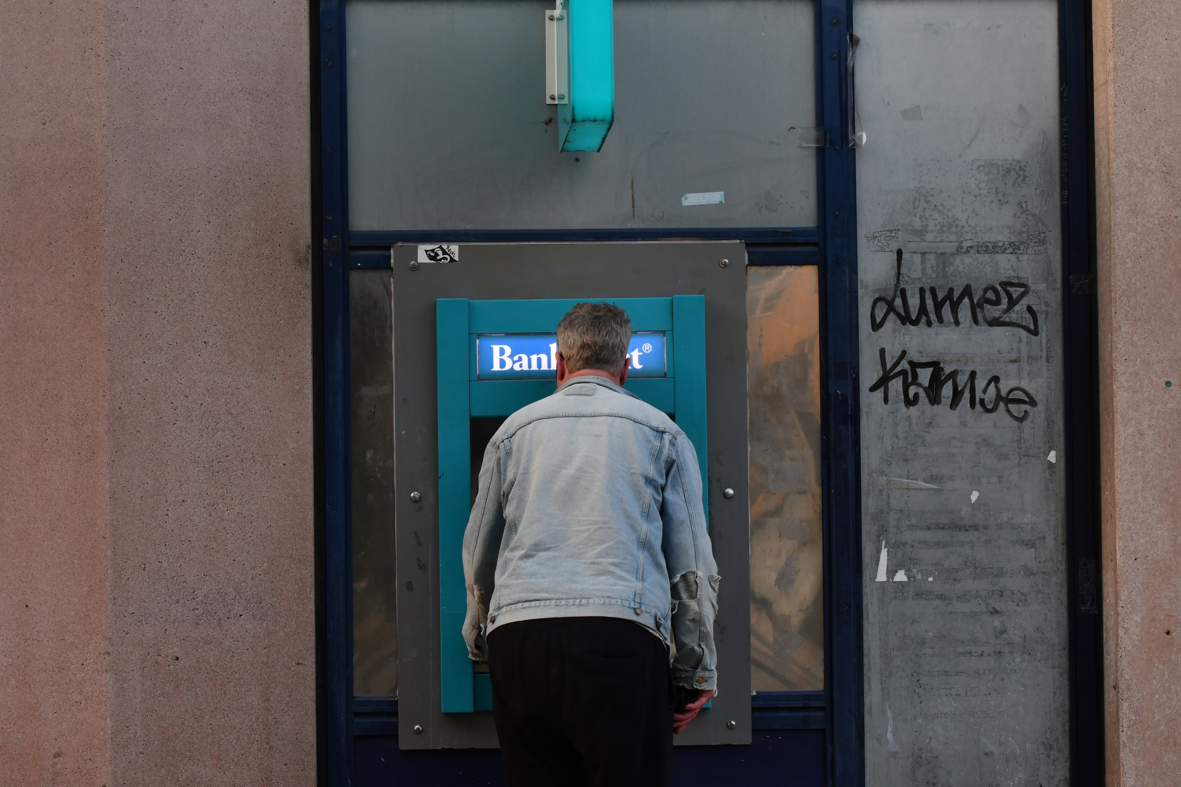 A man seen from behind uses a blue Bankomat cash machine in Malmö.