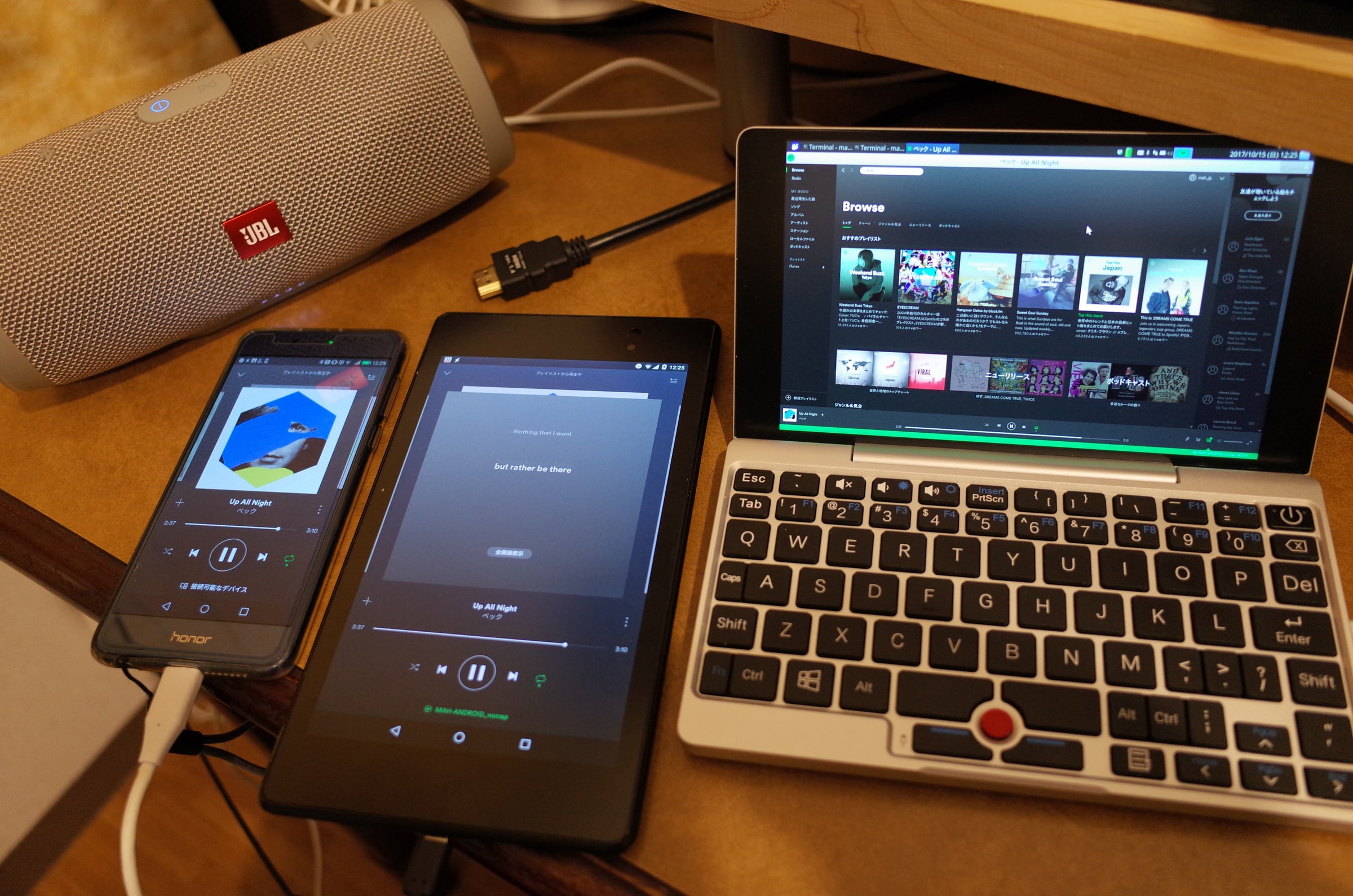 Spotify runs on a smartphone, tablet and small laptop beside a portable speaker.