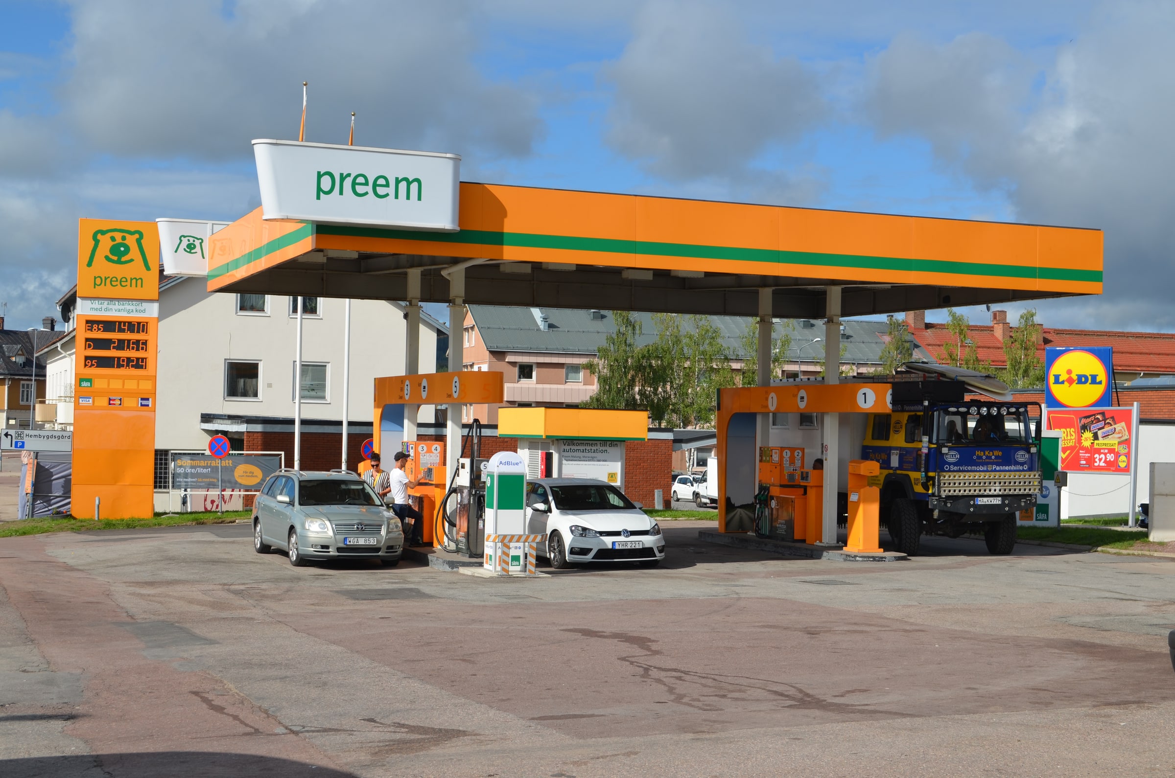 Cars and a truck stand beside fuel pumps under a canopy at a filling station in Malung, Sweden.
