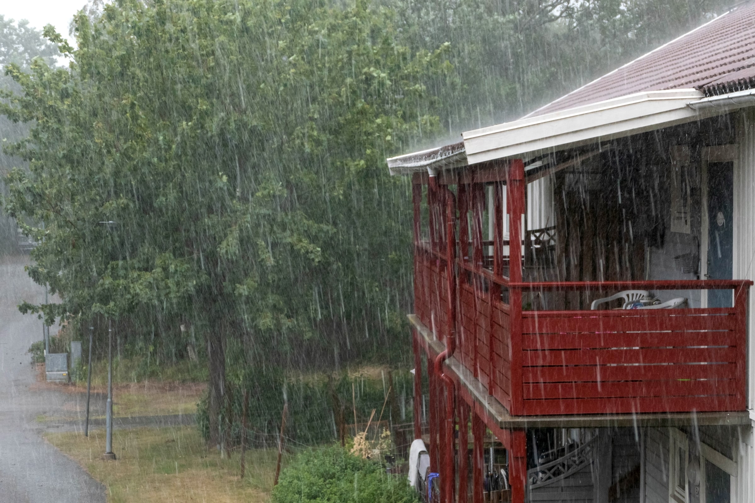 Heavy summer rain falls over houses, trees and a residential street in Brastad, Sweden.