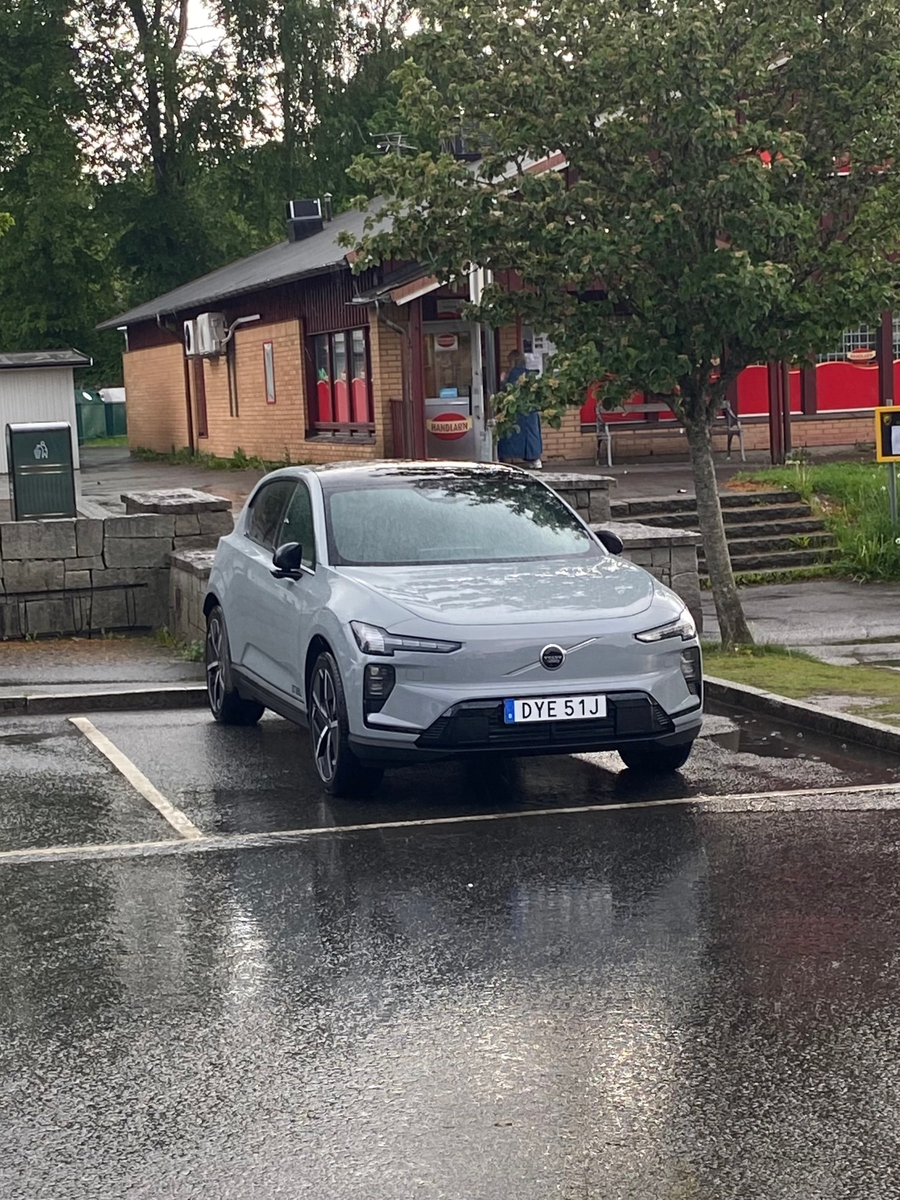 A pale Volvo EX60 test vehicle is parked in a marked space on wet pavement.