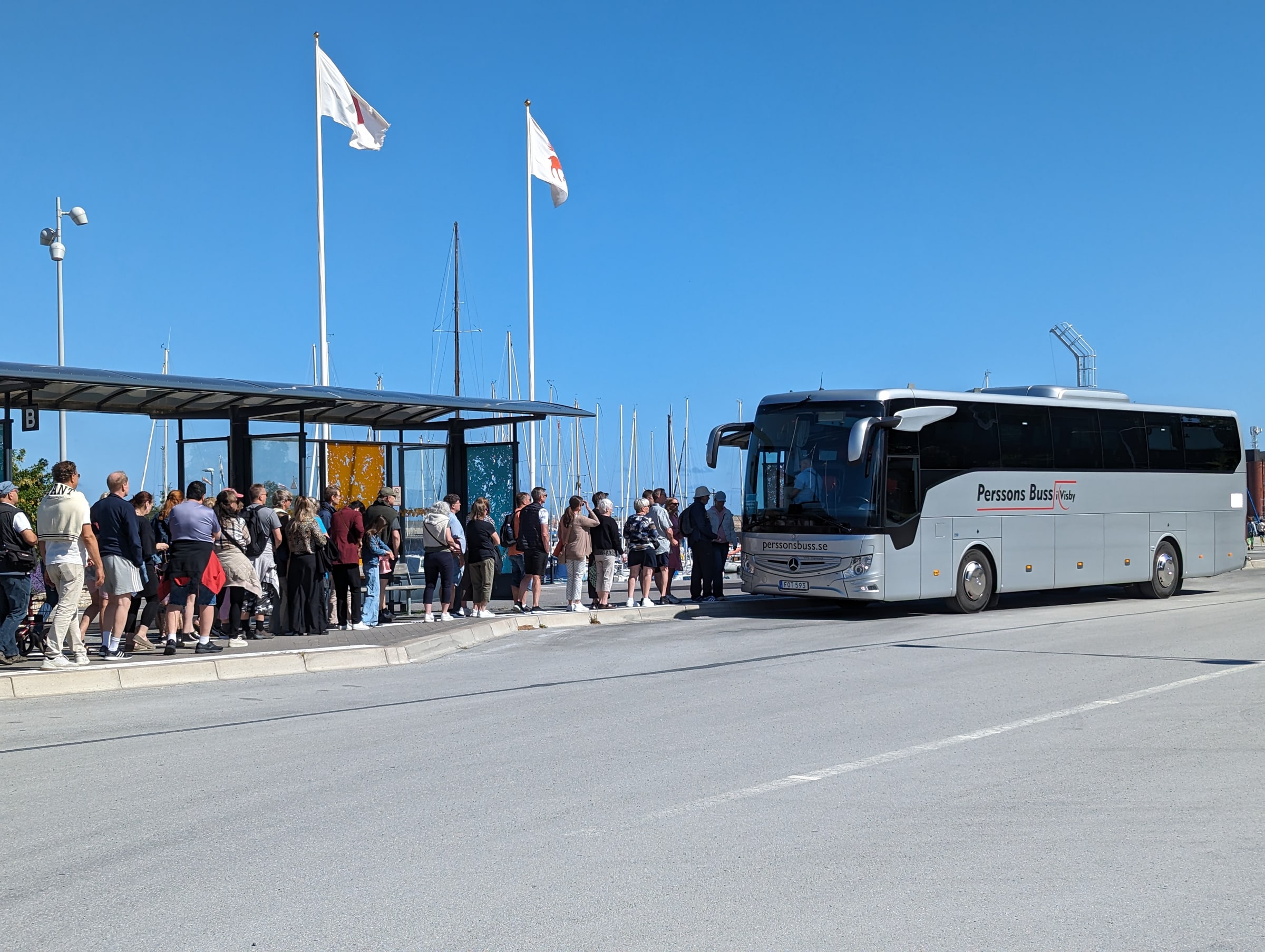 People queue beside a white passenger coach at a sheltered stop in Visby