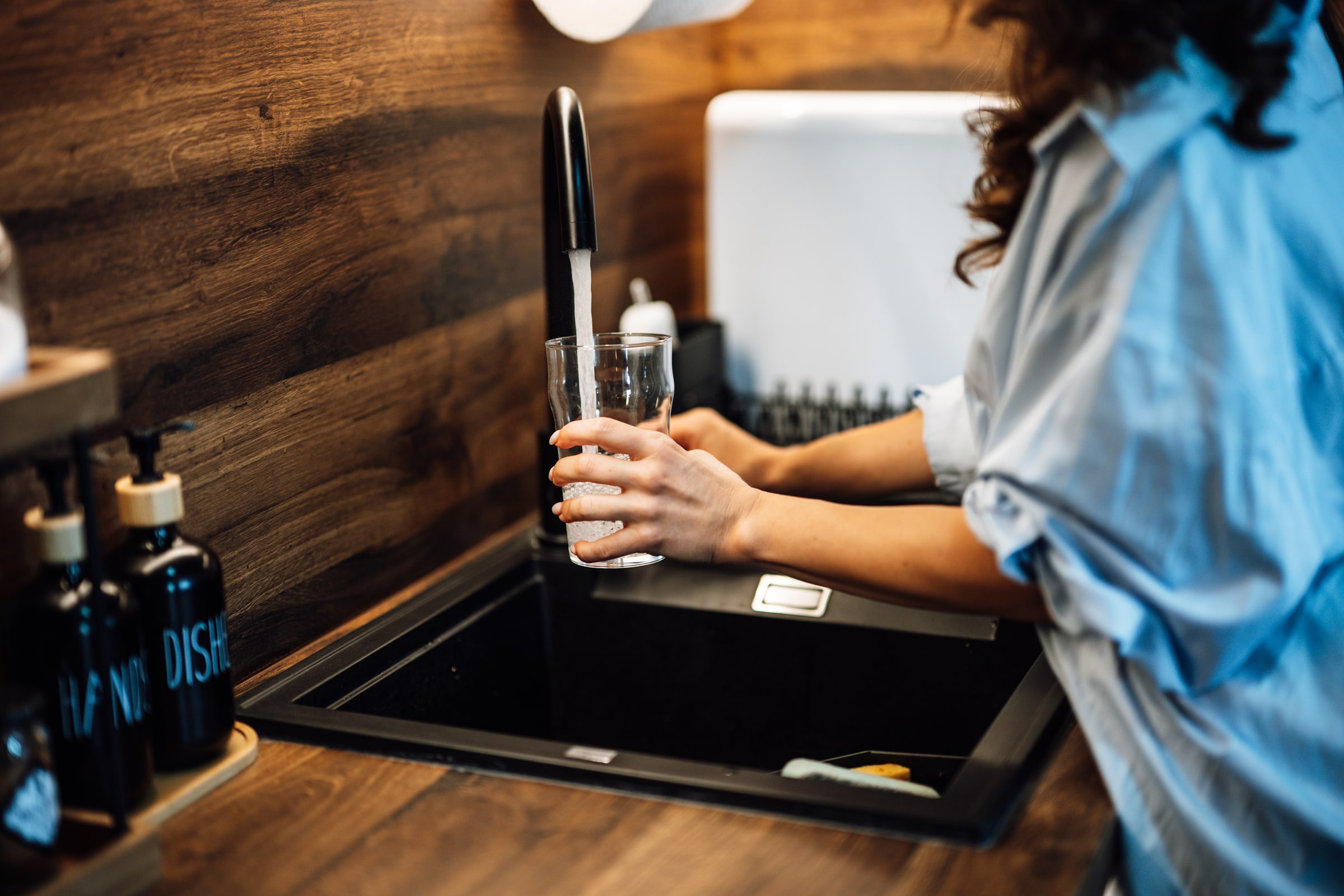 A person fills a drinking glass from a running kitchen tap.