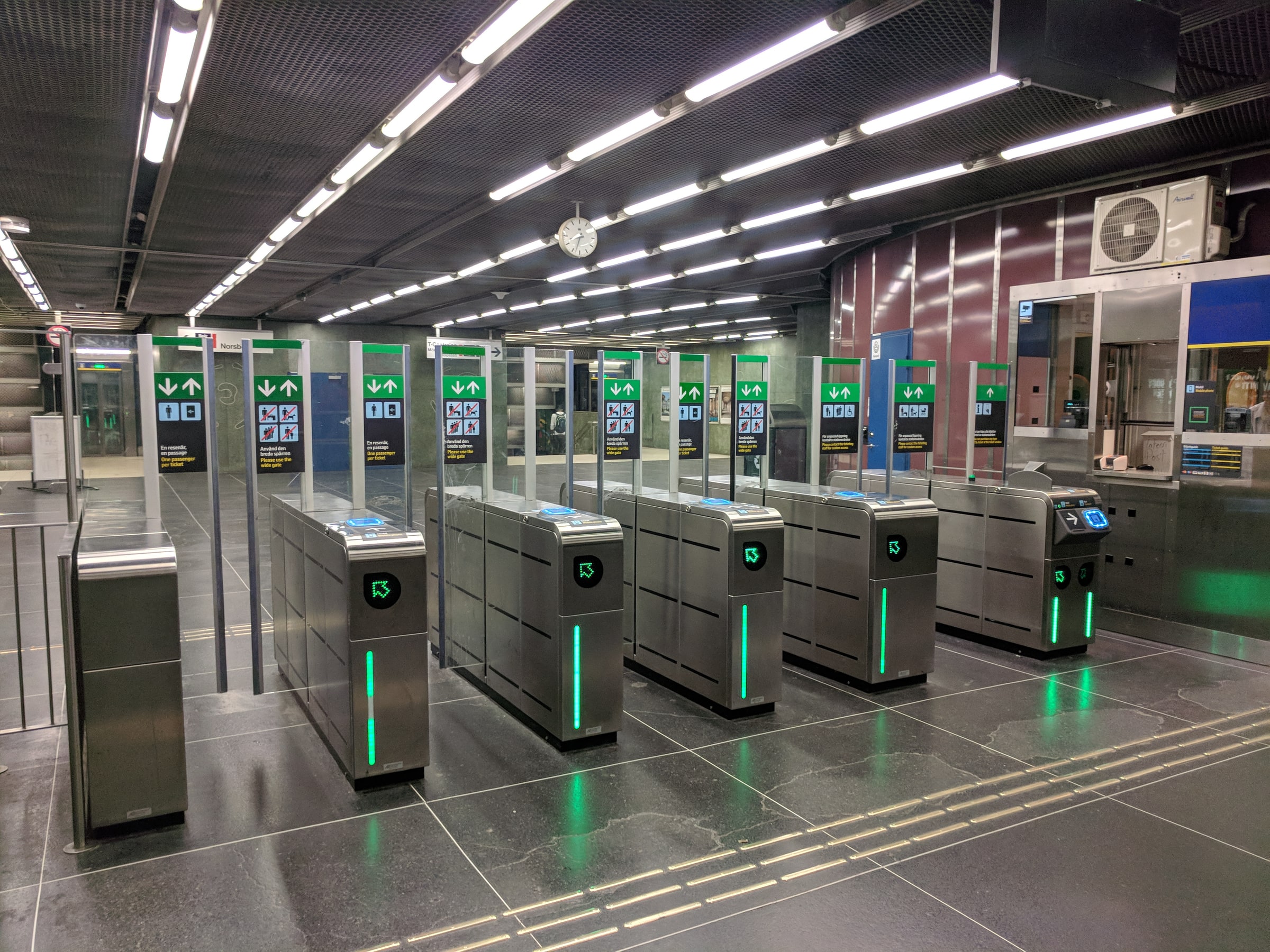 Rows of ticket gates with green indicators inside Alby metro station in Stockholm.