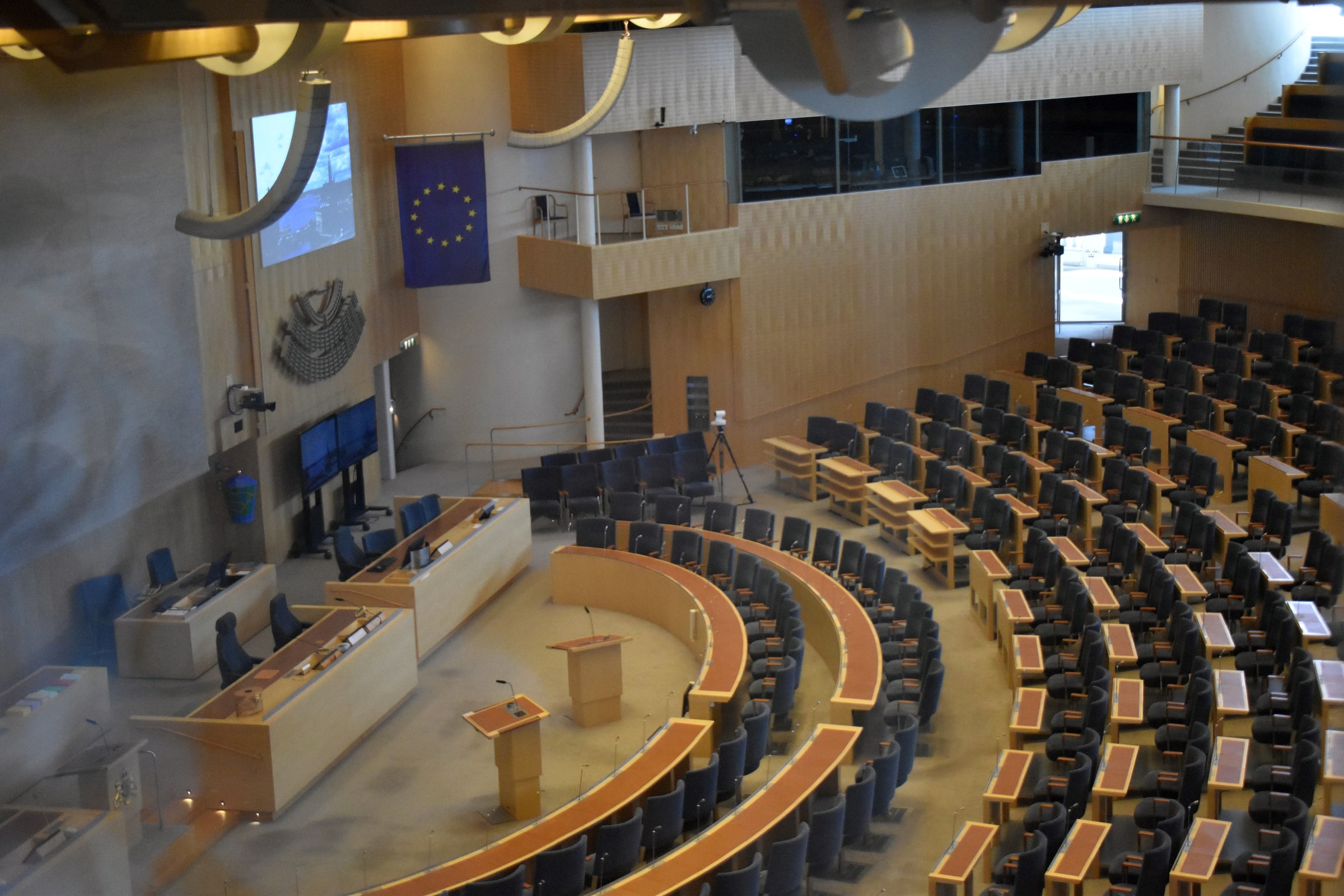 Curved rows of desks and seats face the speaking platforms in the Swedish Parliament chamber.