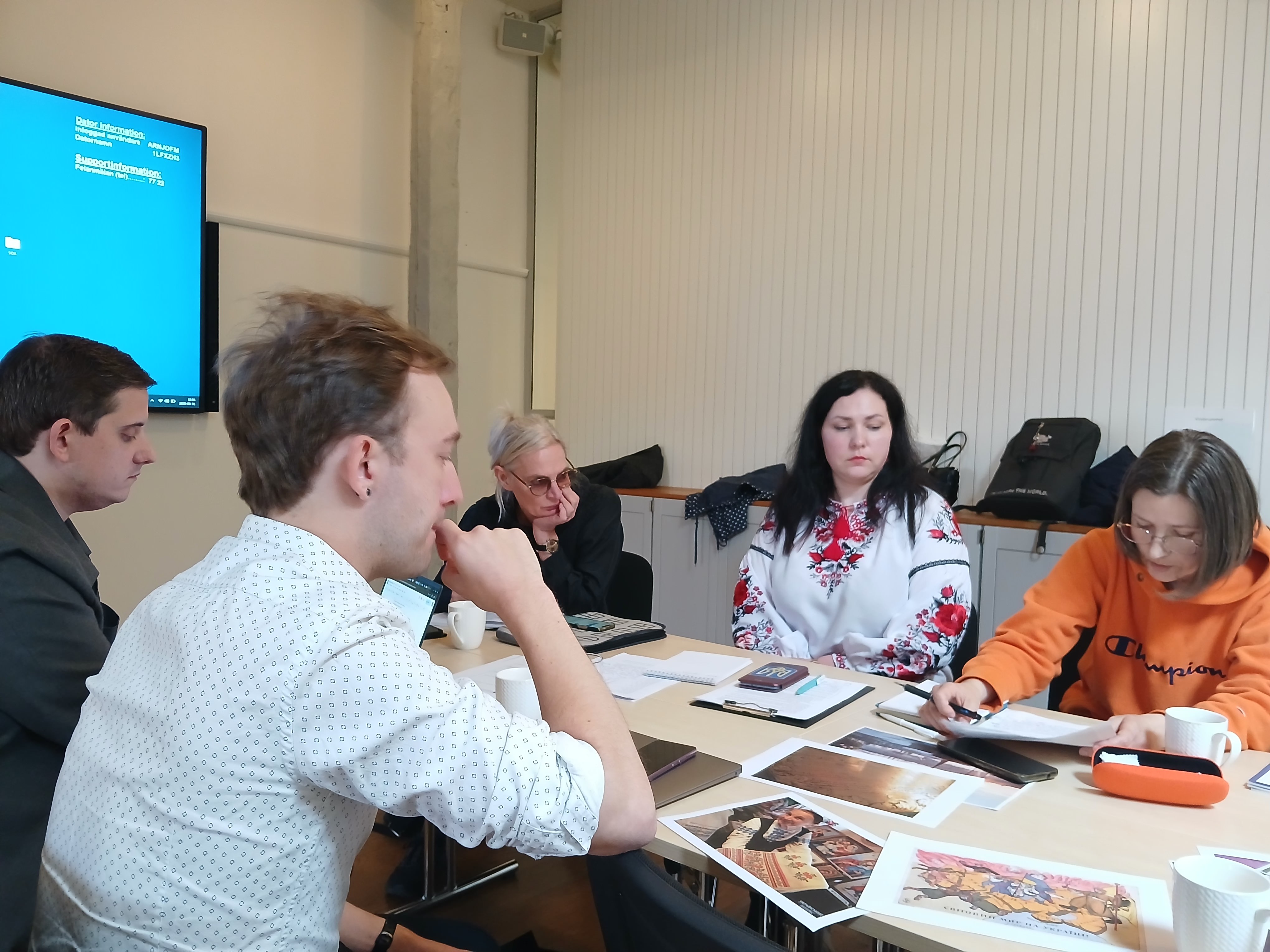 Five people review notes and visual materials around a table during an Open GLAM working meeting in Stockholm.