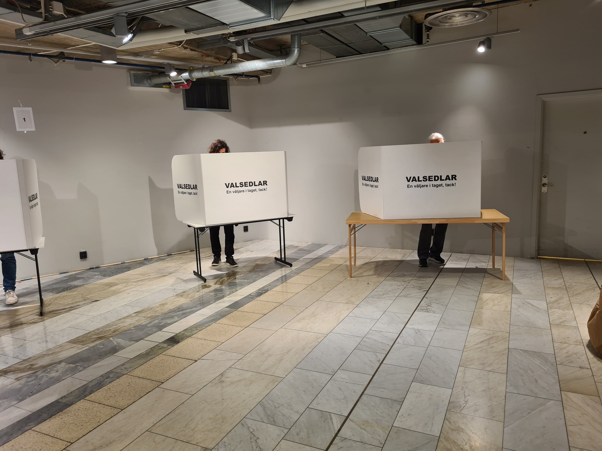 Three voters choose ballot papers behind privacy screens at a Swedish polling station in September 2022.