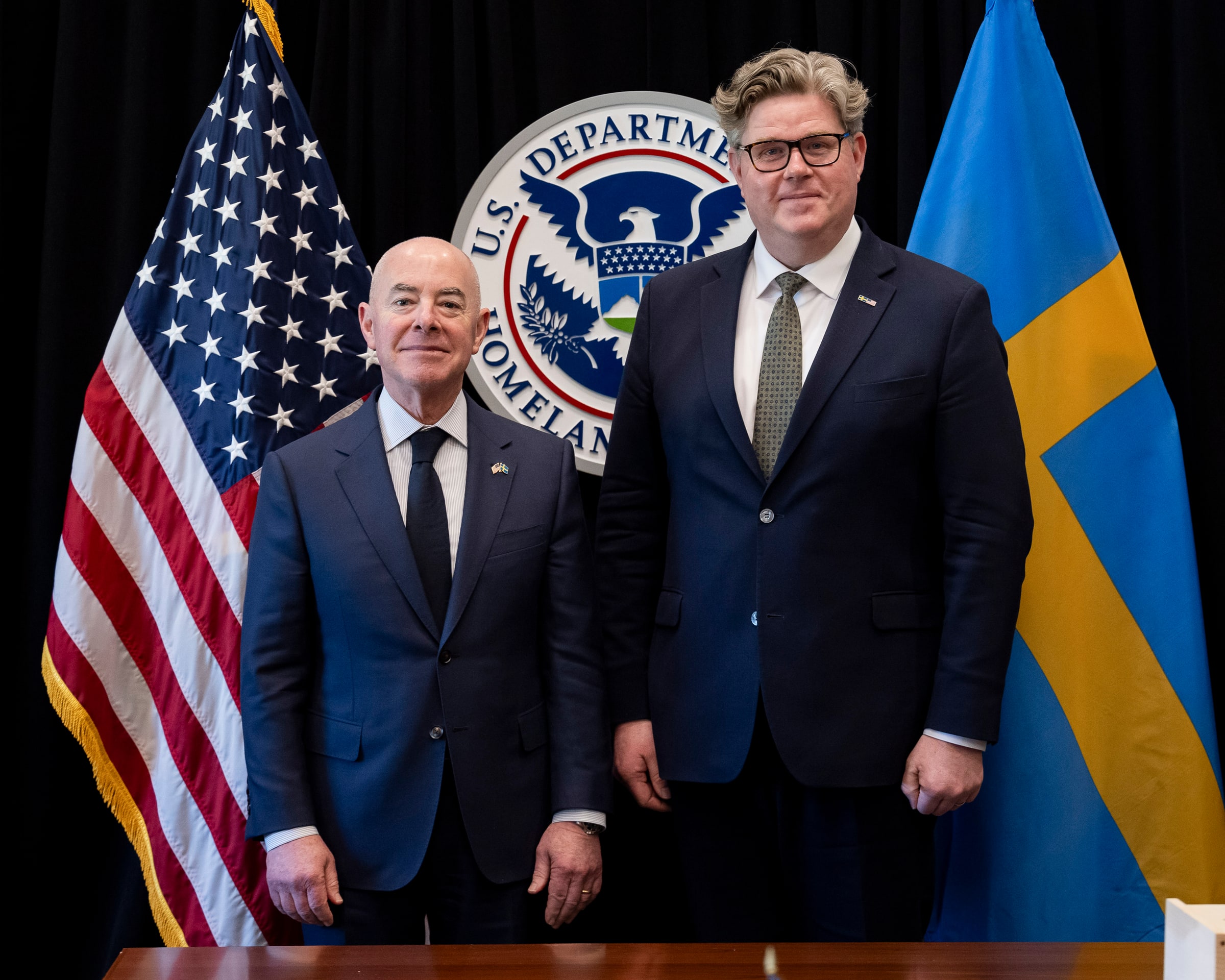Alejandro Mayorkas and Justice Minister Gunnar Strömmer stand beside the US and Swedish flags.