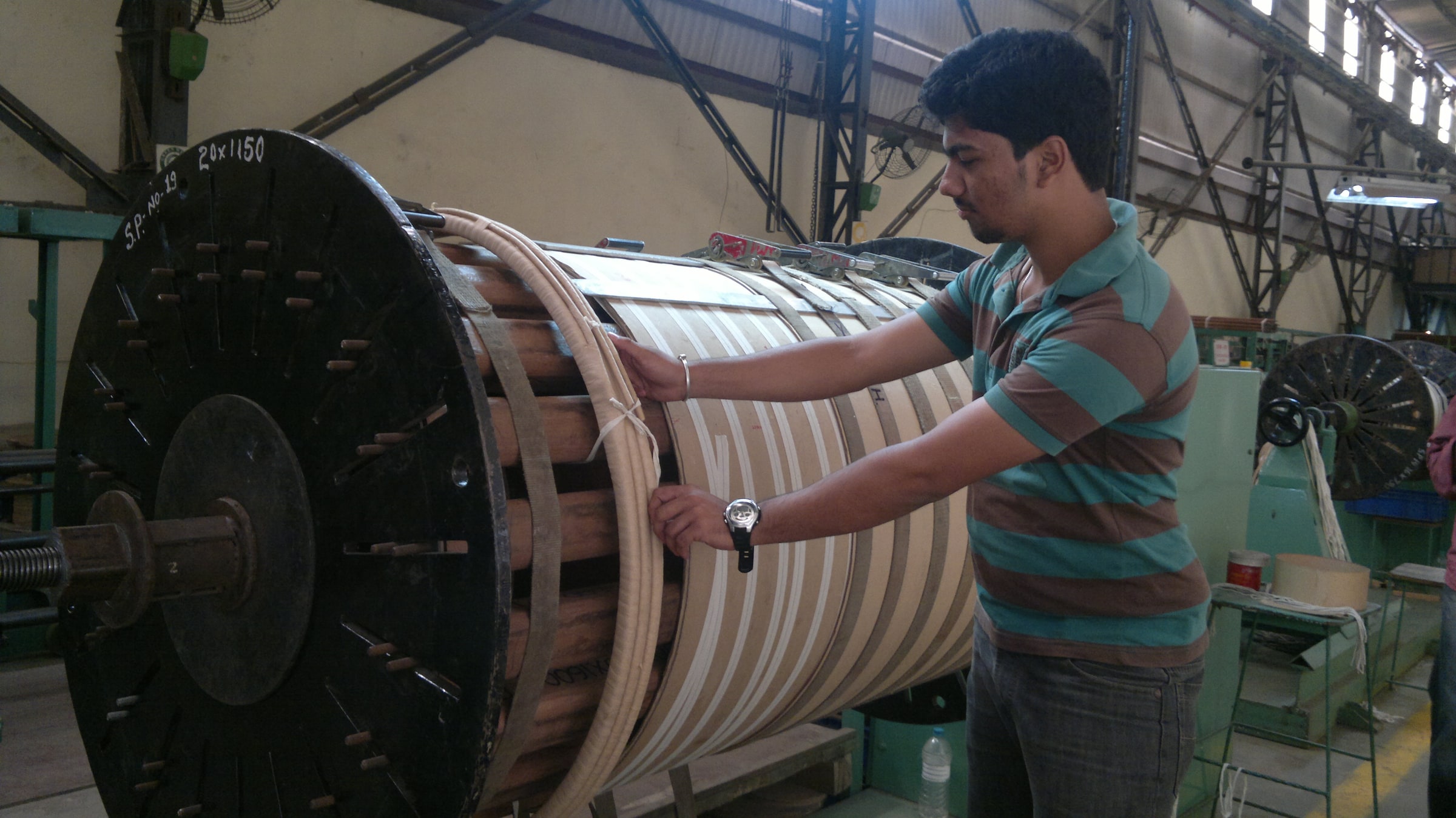 An engineer handles winding material on a large power-transformer winding machine in an industrial workshop.
