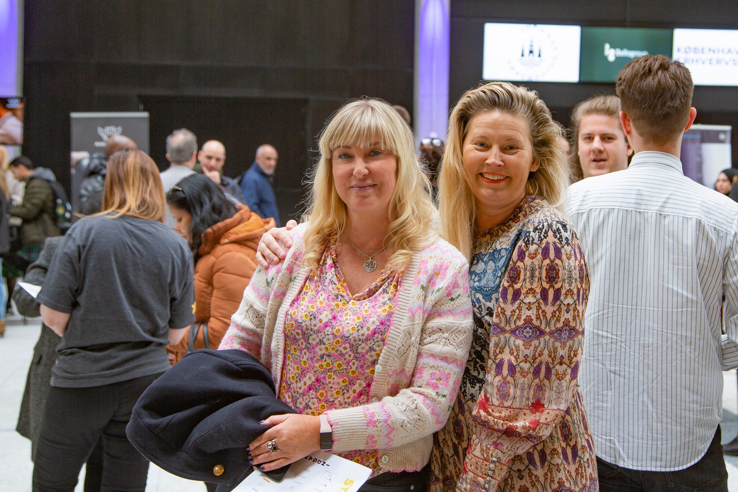 Two adult women stand among attendees at a Danish-Swedish job fair in Copenhagen.