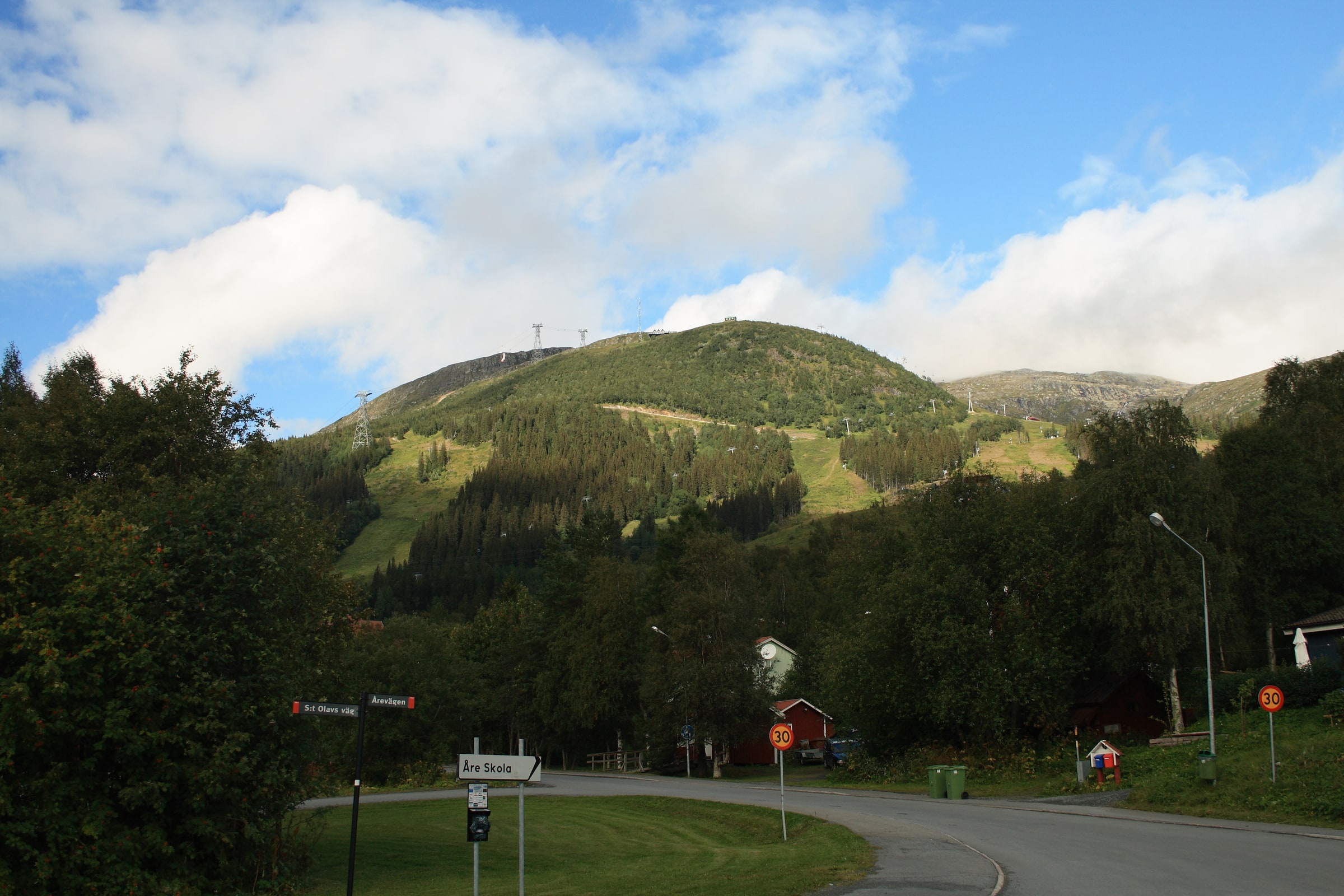Åreskutan rises above green summer slopes and a road in Åre village.