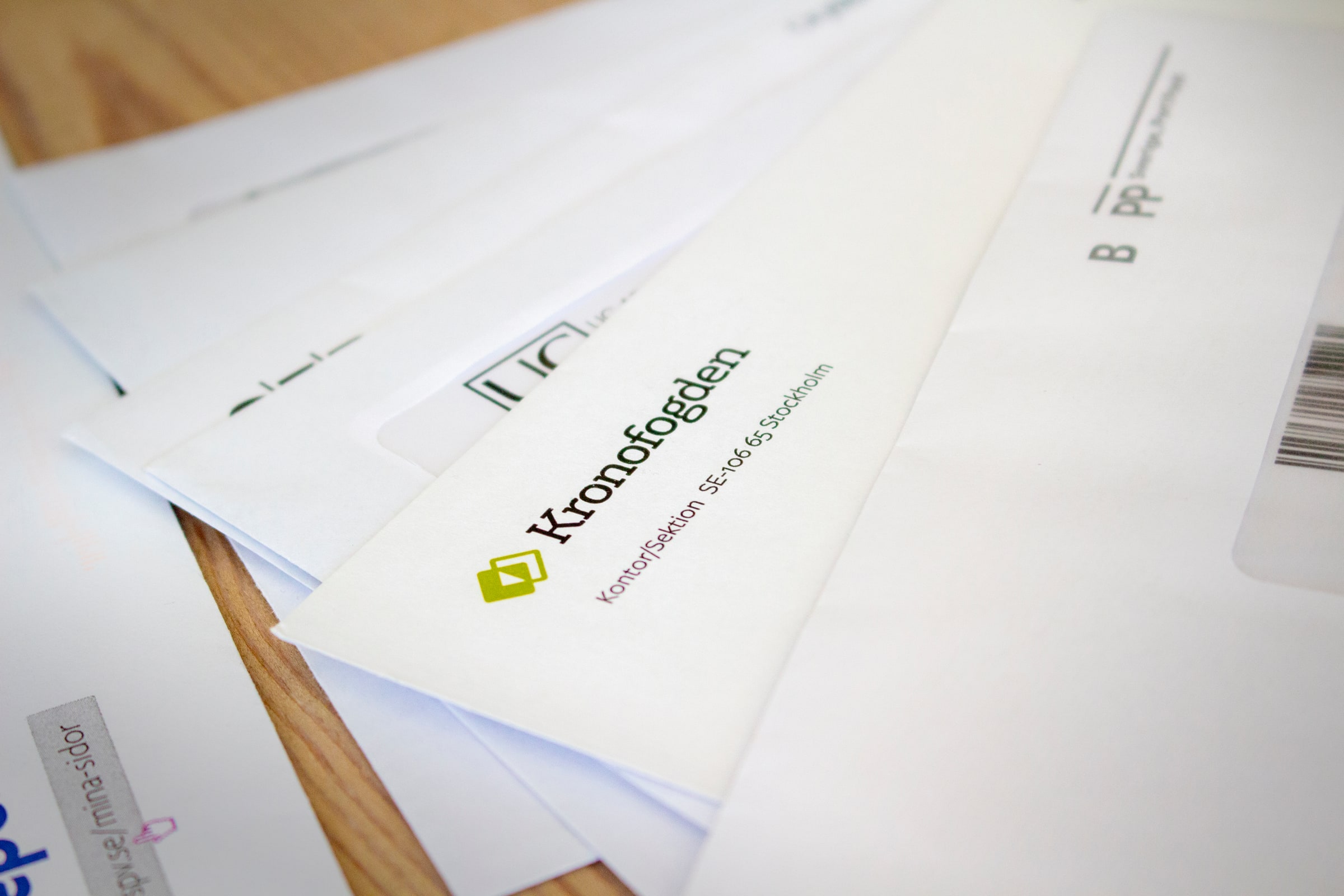 Several official-looking envelopes on a wooden table, with a Kronofogden envelope prominent in the foreground.