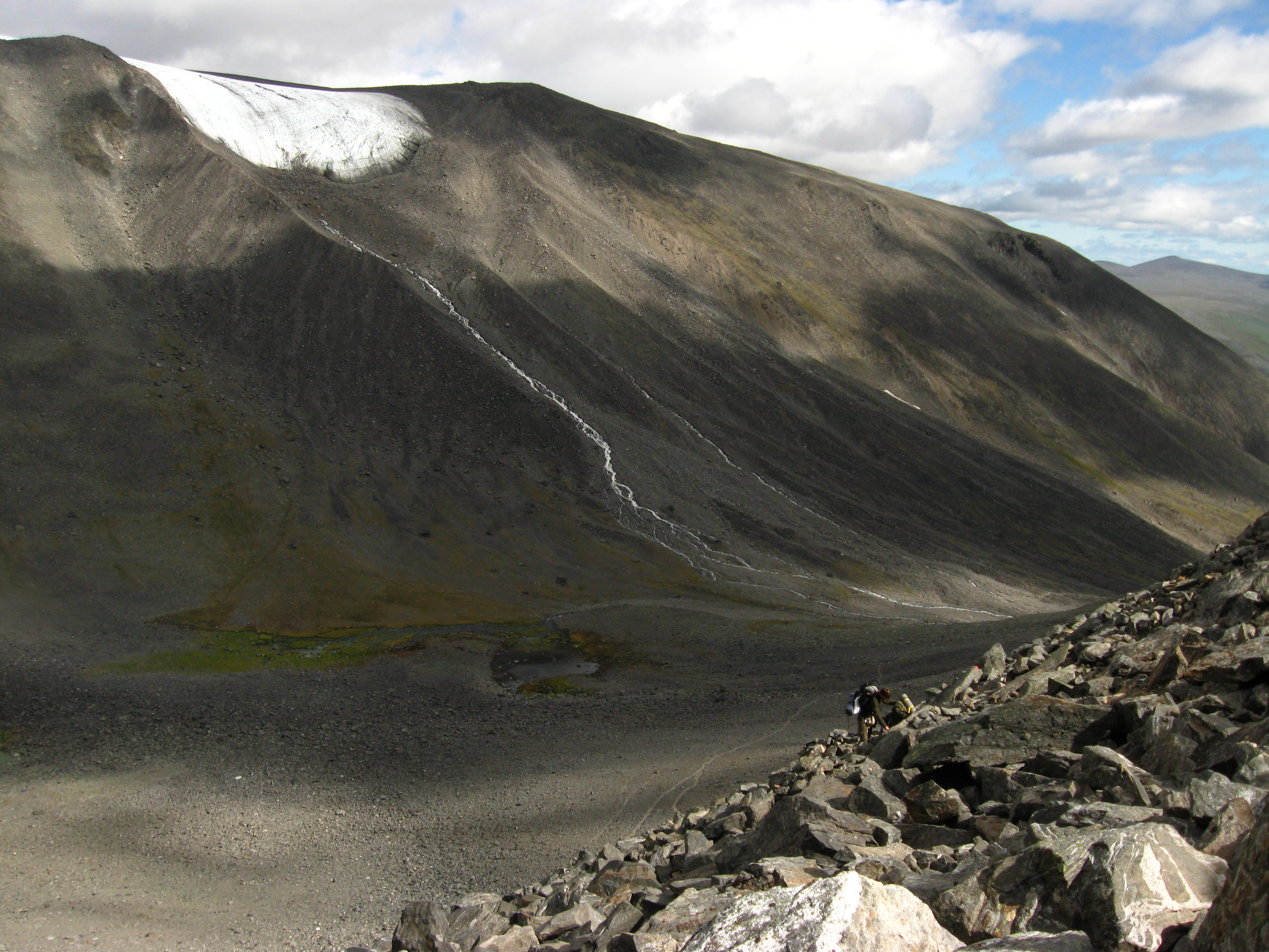 A hiker scrambles across loose rocks on the exposed Västra leden route at Kebnekaise.