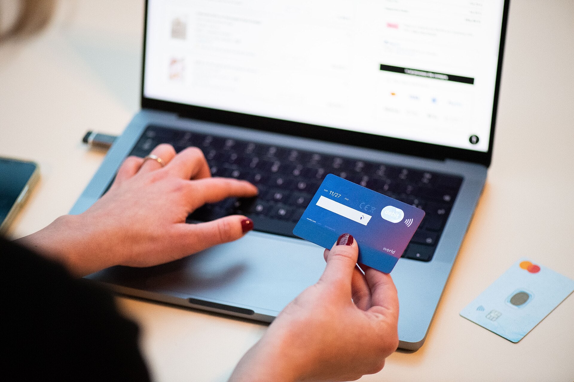 A person holds a bank card while using a laptop for online shopping.