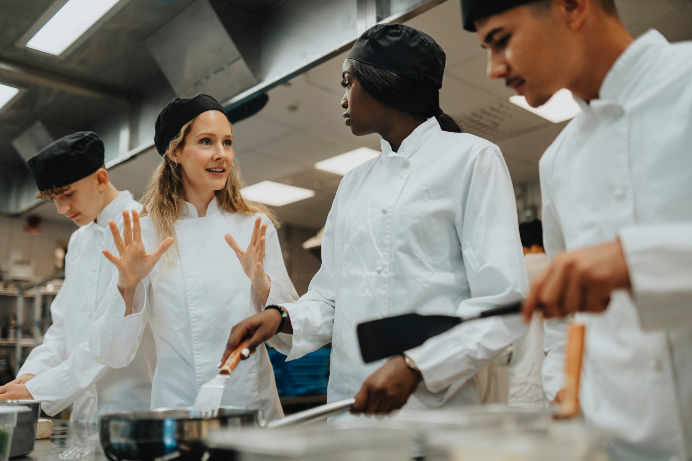 A mentor explains a cooking task to learners in a Swedish kitchen.
