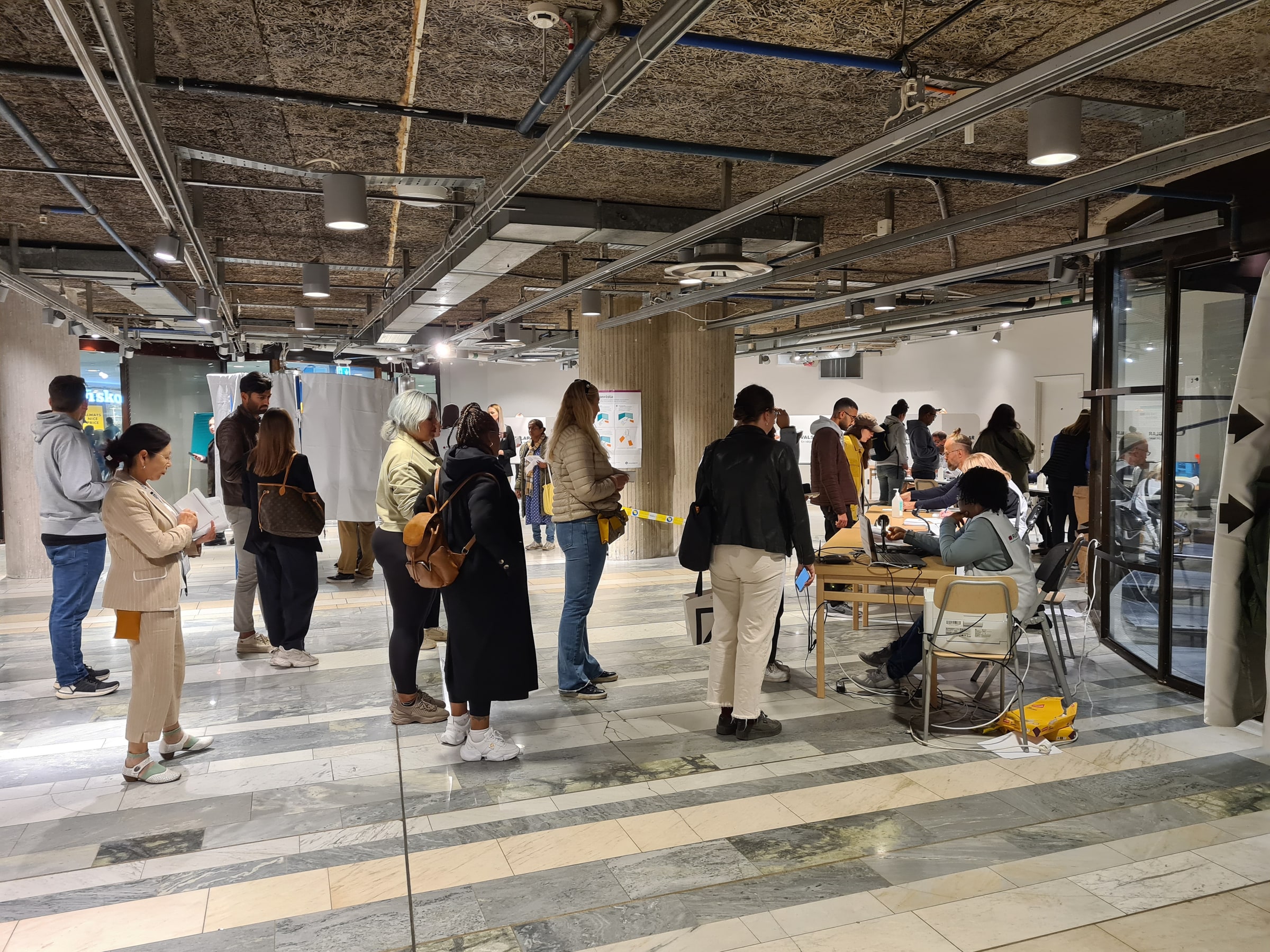 Adults queue inside a Swedish advance-voting venue.
