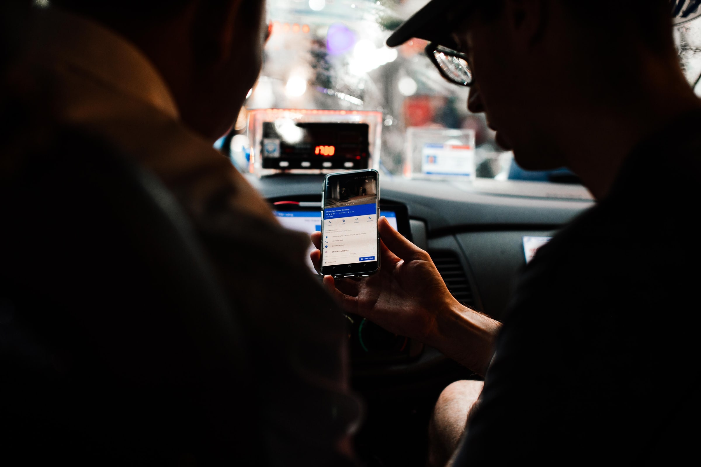 Two people look at a smartphone inside a car at night.