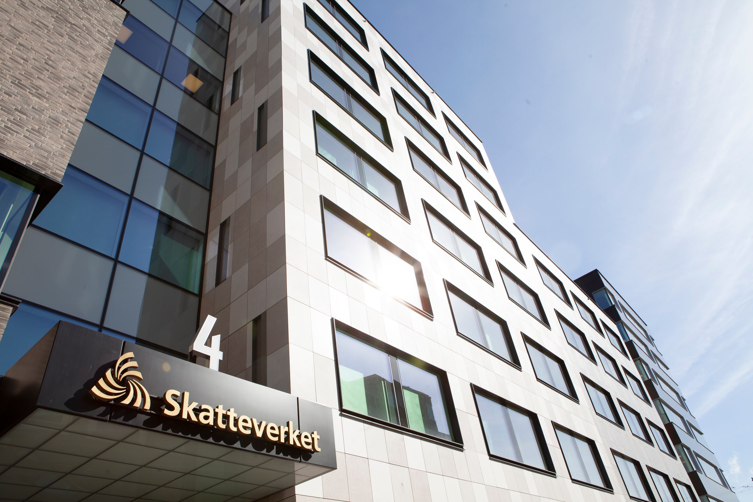 An upward daylight view of Skatteverket's Kronan office facade and entrance sign in Sundbyberg.